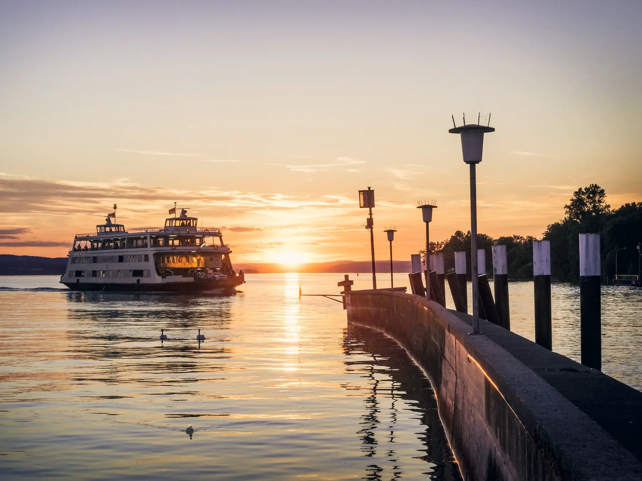 Fahrgastschiff und Autofähre bei stimmungsvollem Sonnenuntergang auf dem Bodensee an einer Anlegestelle