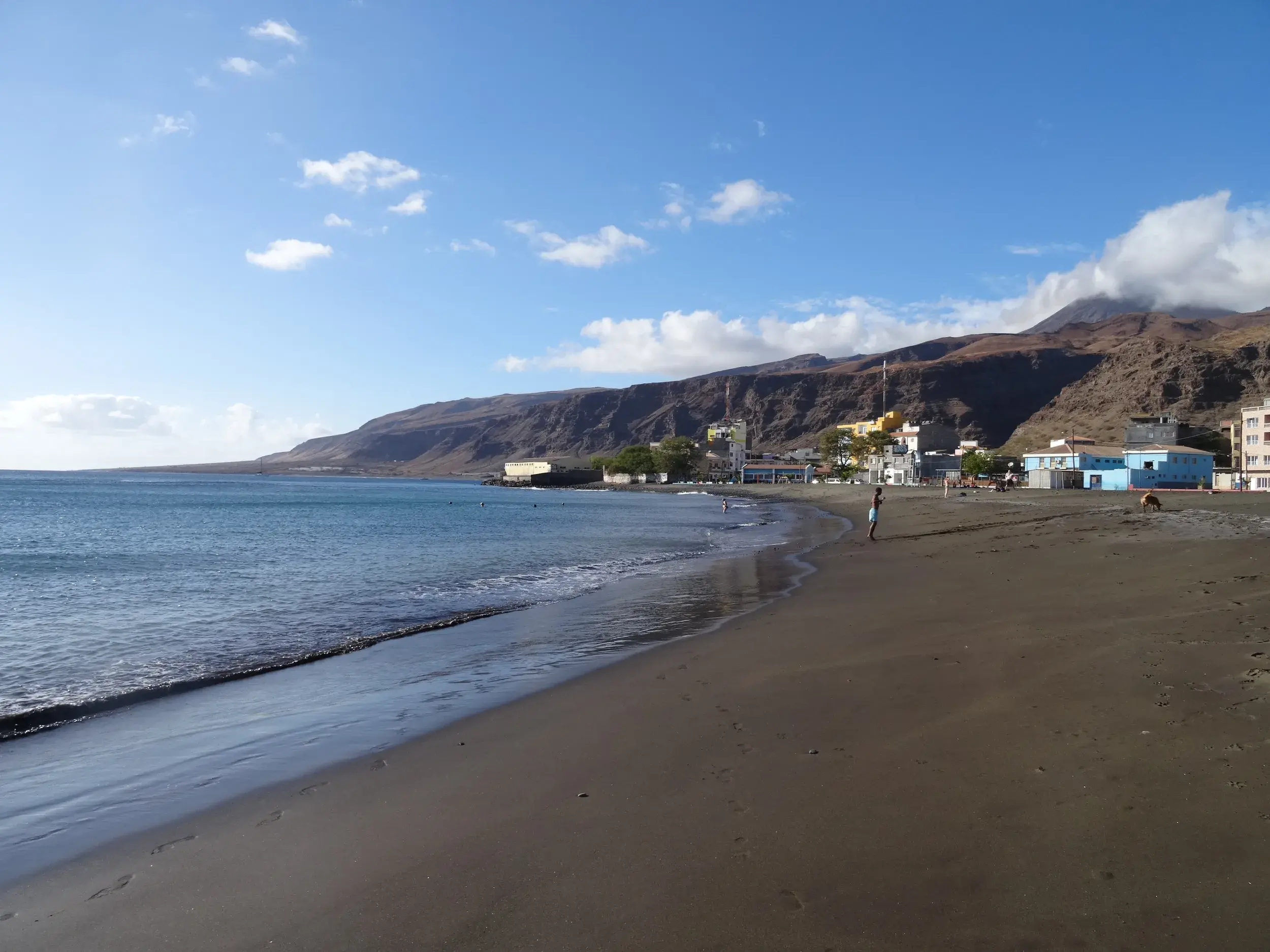 Weitläufiger, dunkler Sandstrand in Mindelo auf São Vicente, im Hintergrund erheben sich die Küstenberge der Kapverden.