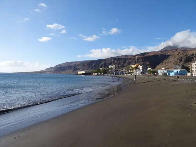 Weitläufiger, dunkler Sandstrand in Mindelo auf São Vicente, im Hintergrund erheben sich die Küstenberge der Kapverden.