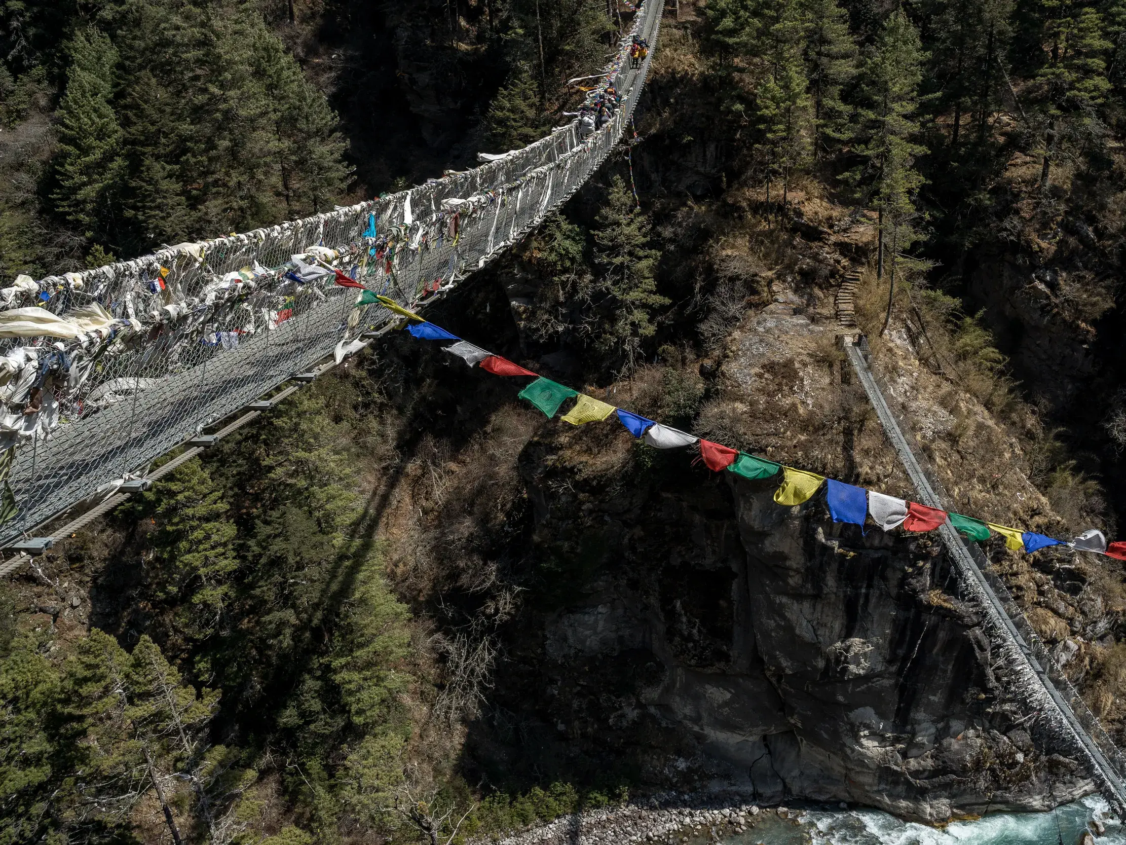 Wanderer queren die hohe, mit Gebetsfahnen geschmückte Hillary-Hängebrücke über einer tiefen Schlucht auf dem Trek nach Namche Bazar.