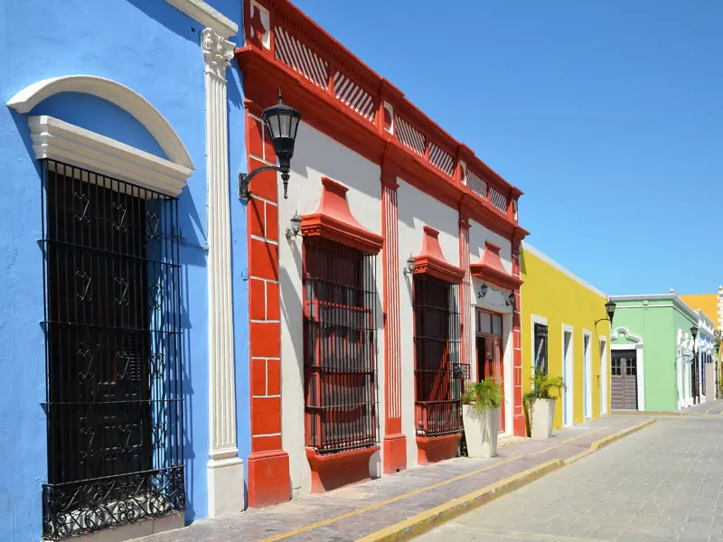 Farbenfrohe Kolonialhäuser in blau, rot und gelb säumen eine sonnige, leere Gasse in der Kolonialstadt Campeche in Mexiko.