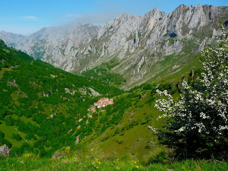 Weitblick beim Wandern auf das Bergdorf Sotres, das in einem grünen Tal vor den schroffen Kalksteingipfeln der Picos de Europa liegt.