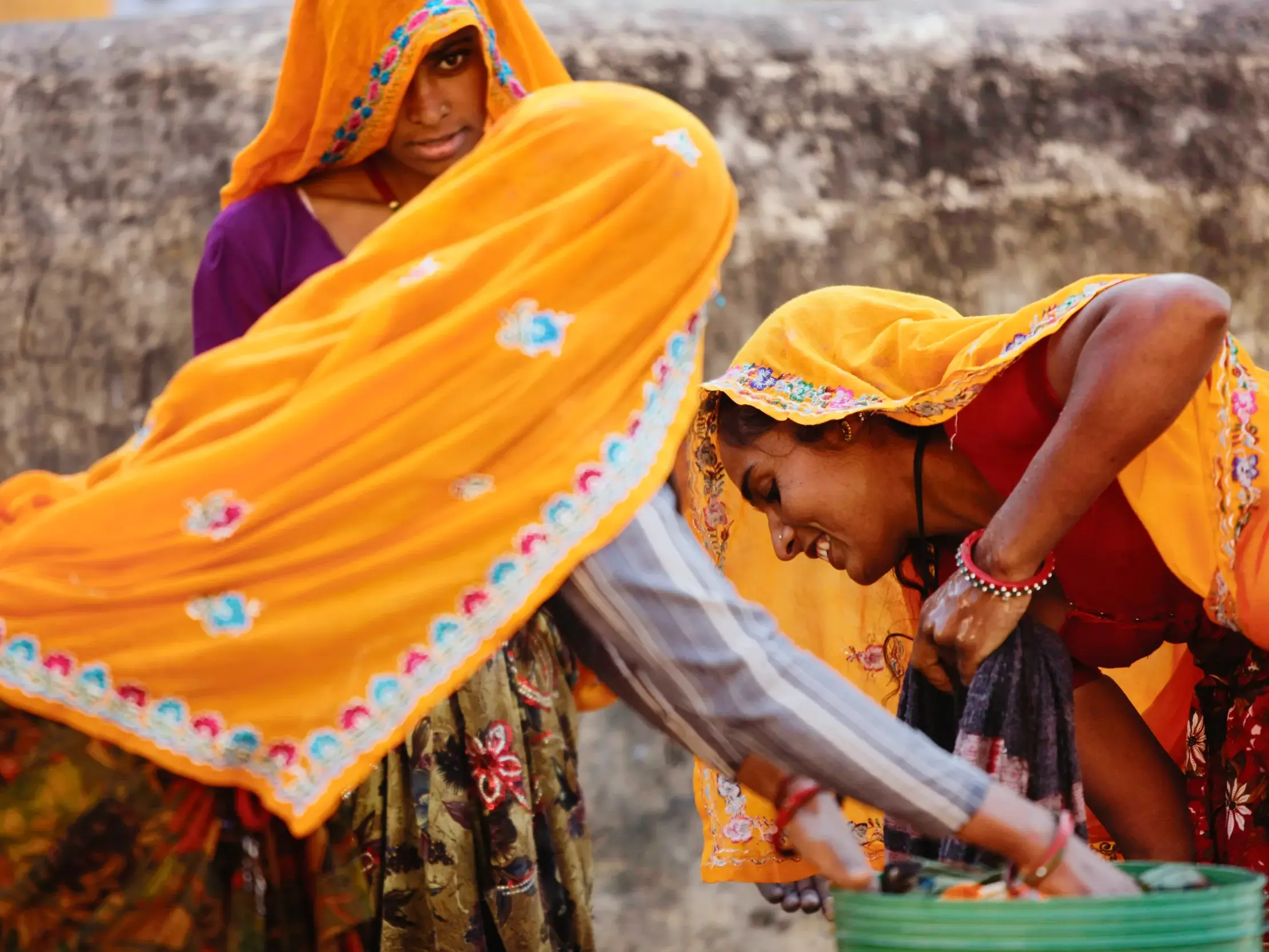 Drei indische Frauen in leuchtend-bunten Saris waschen Wäsche – eine authentische Begegnung in Rajasthan.