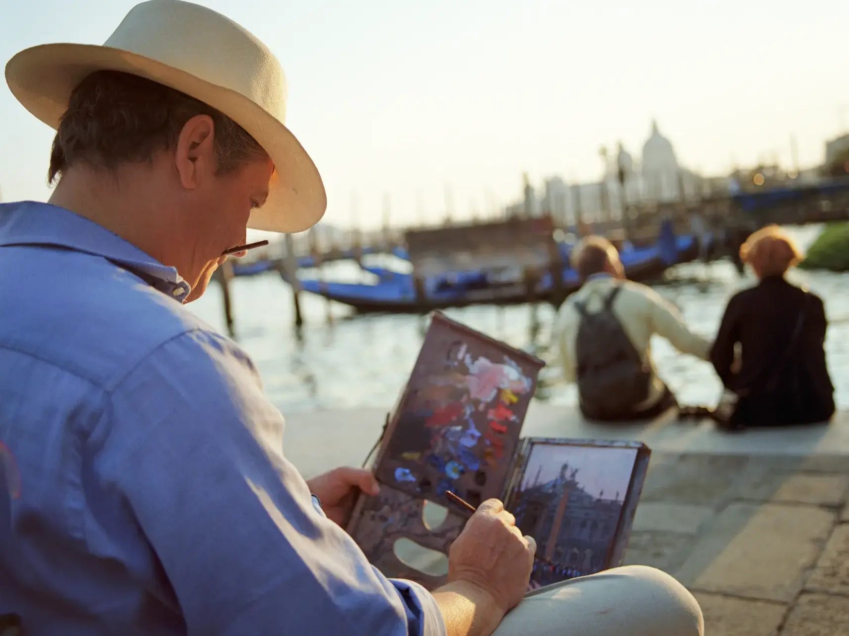 Ein Maler mit Hut fängt die stimmungsvolle Atmosphäre am Canal Grande in Venedig bei Sonnenuntergang auf seiner Leinwand ein.