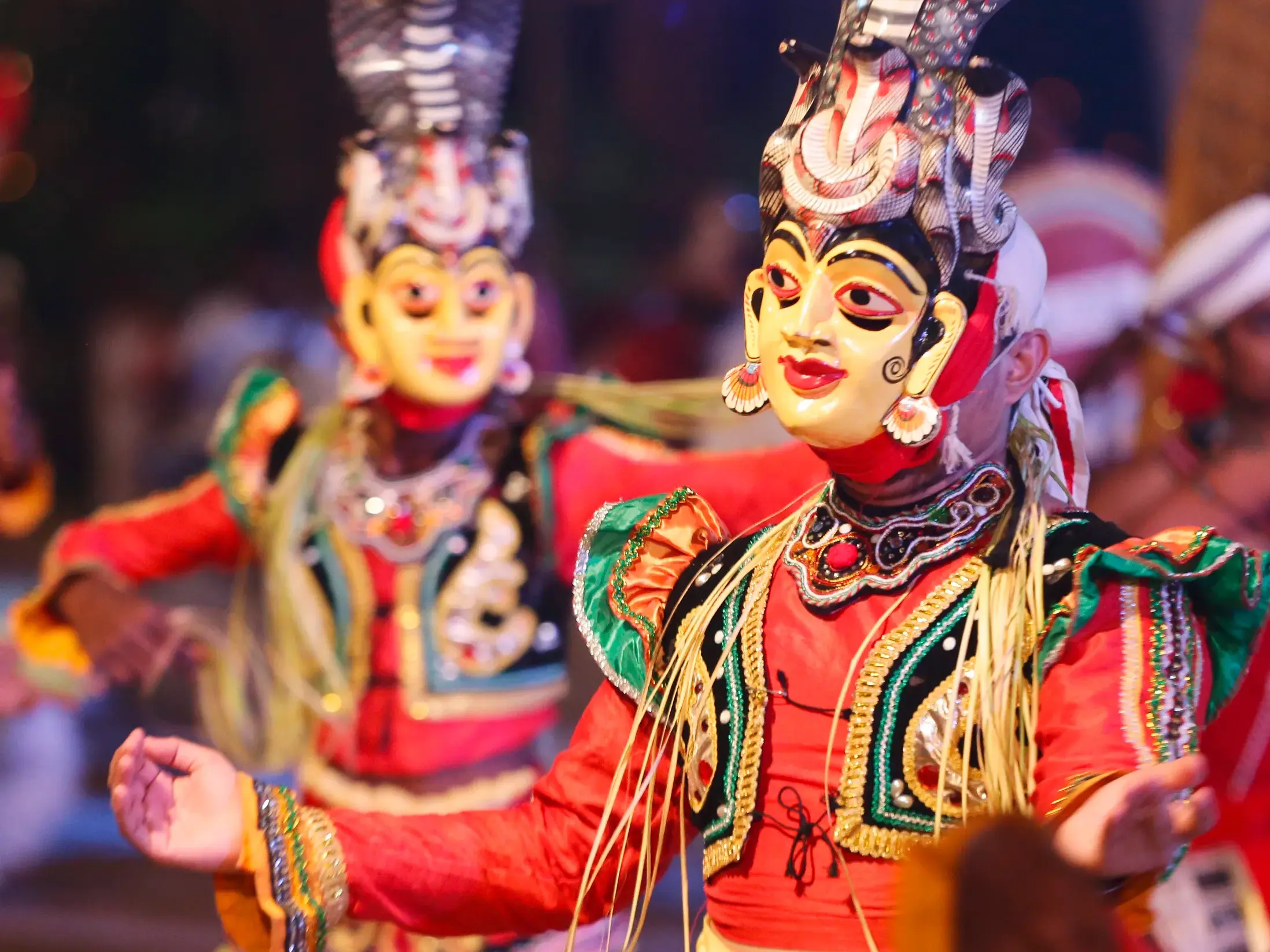 Zwei Tänzer in farbenprächtigen Kostümen und Masken führen nachts die traditionellen Kandyan Dances in Kandy, Sri Lanka auf.