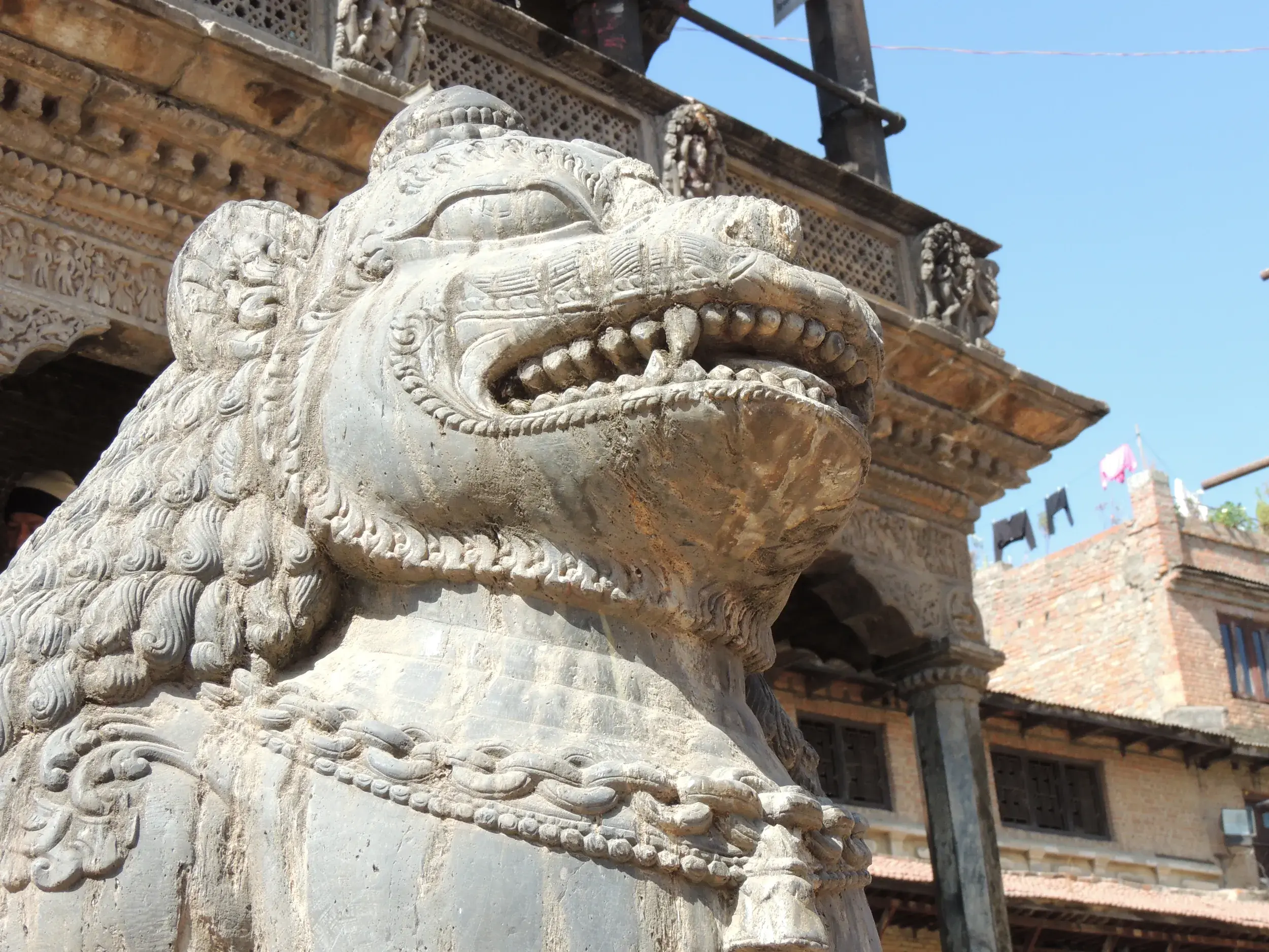 Steinerne Wächterfigur mit spitzen Zähnen bewacht den Eingang eines kunstvoll verzierten Tempels in der Königsstadt Bhaktapur.