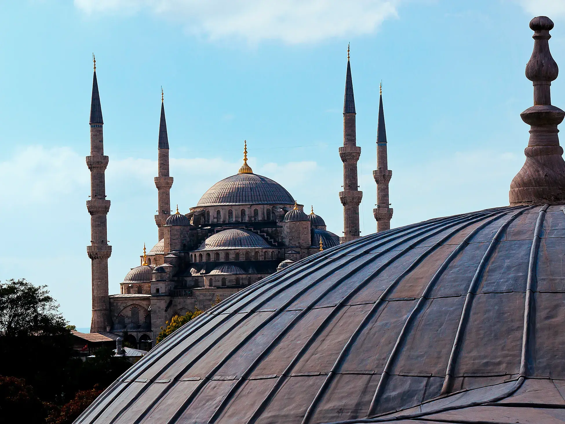 Blick über eine metallene Kuppel auf die prächtige Blaue Moschee mit ihren Minaretten in Istanbul unter blauem Himmel.