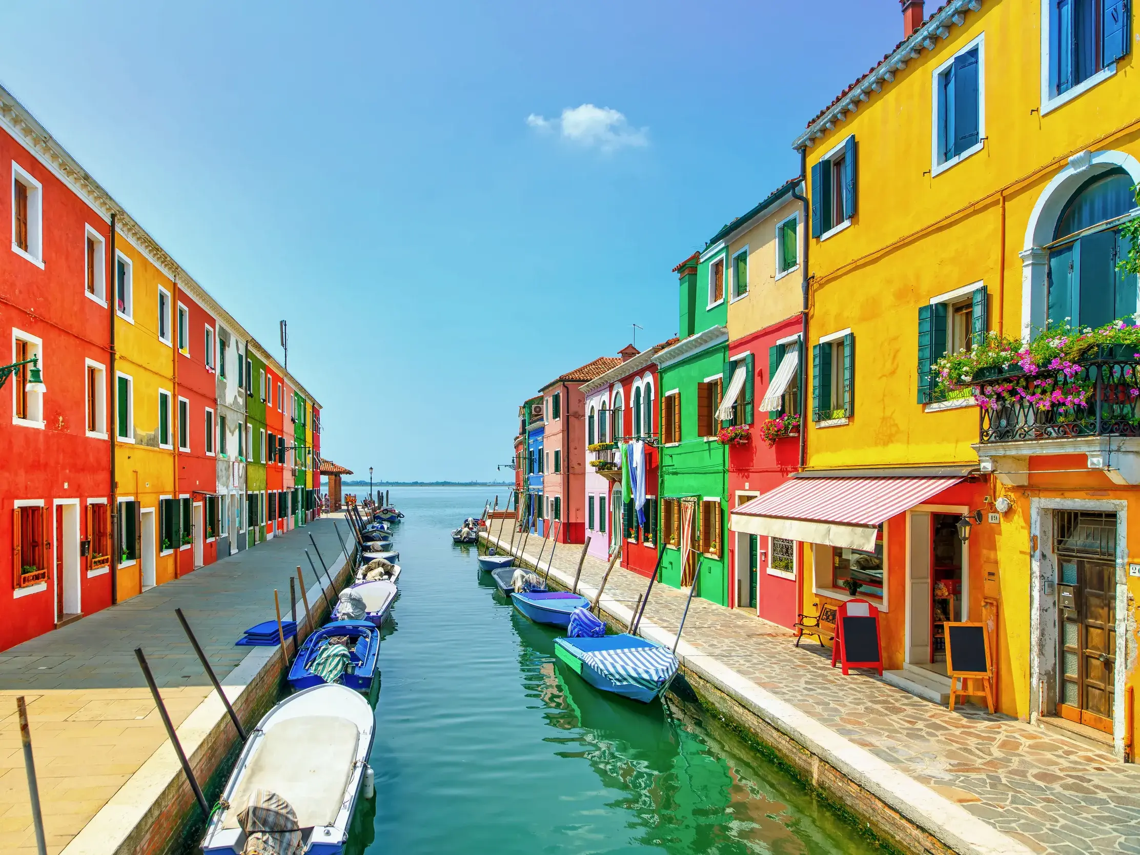 Farbenfrohe Häuser in Rot, Gelb und Grün säumen einen Kanal auf der venezianischen Insel Burano bei Venedig.