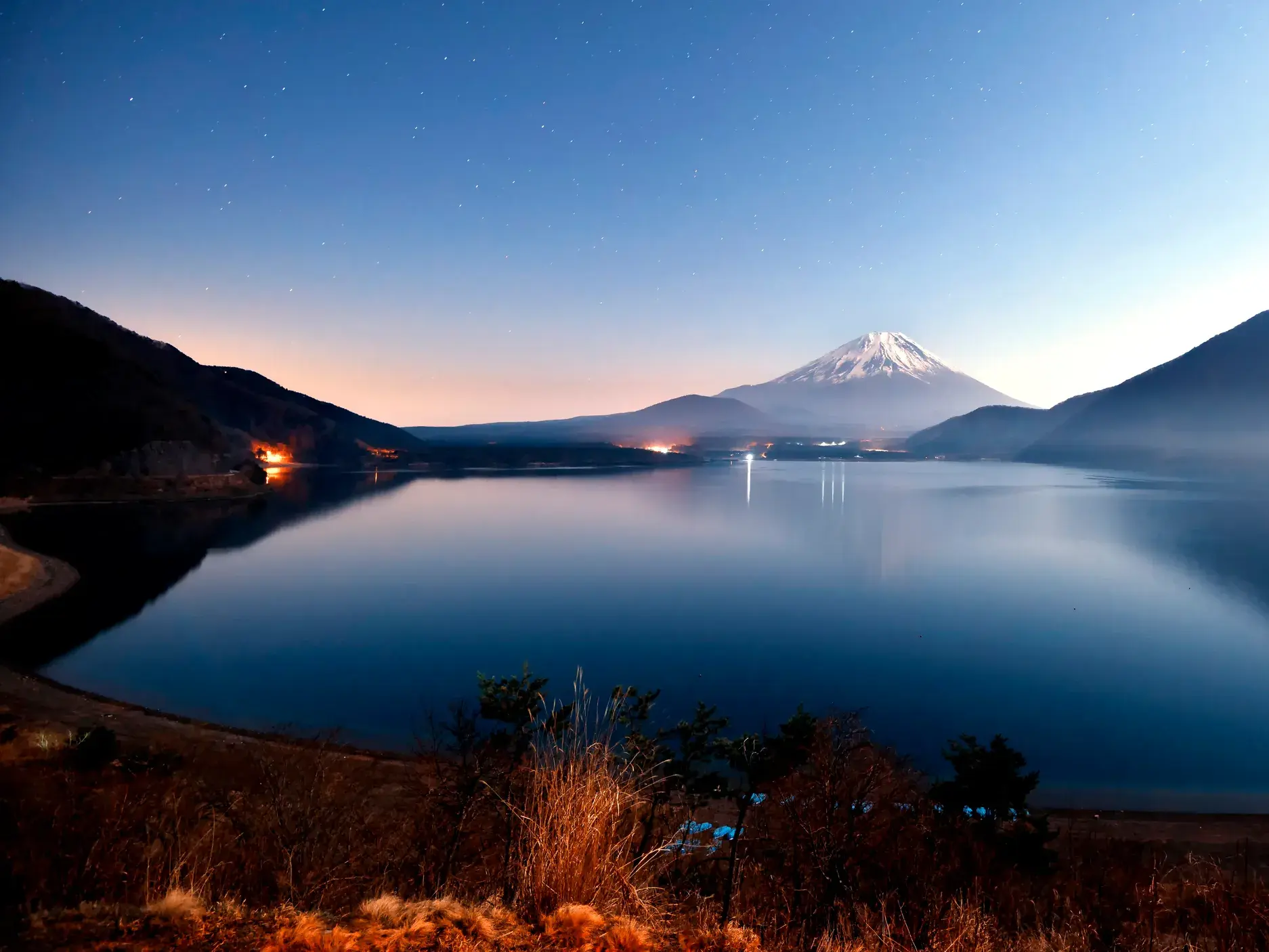 Der schneebedeckte Vulkan Fuji-san spiegelt sich bei Dämmerung im ruhigen Kawaguchi-See unter einem klaren Sternenhimmel.