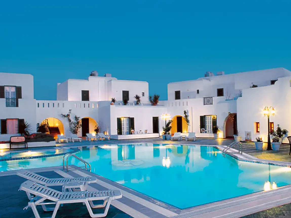 Der beleuchtete Pool des Hotels Astir auf Naxos mit den weißen Gebäuden im Kykladenstil in der Abenddämmerung.
