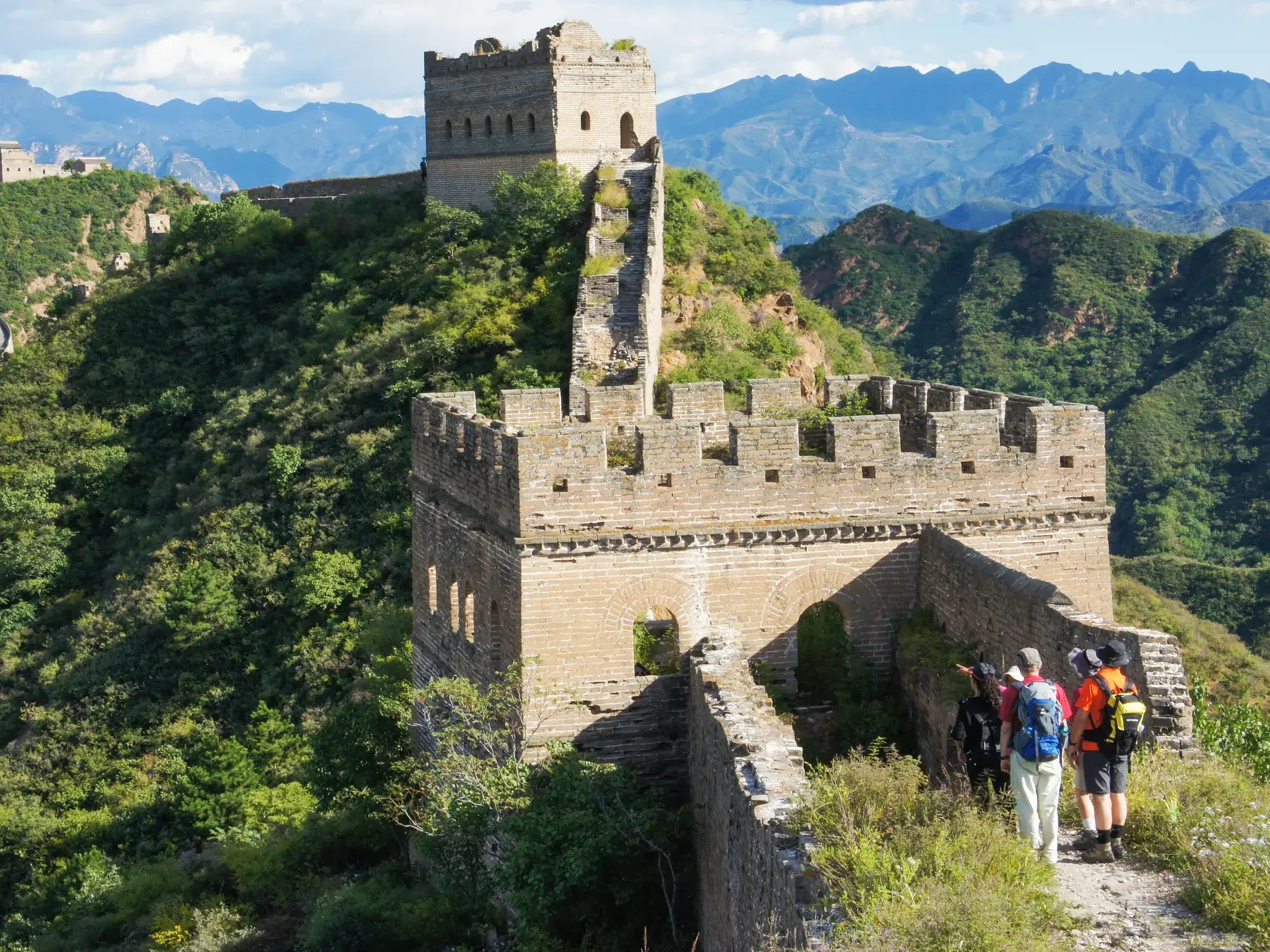 Kleine Hauser-Wandergruppe erkundet auf einem Pfad die Chinesische Mauer bei Jinshanling vor einer grünen Bergkulisse.