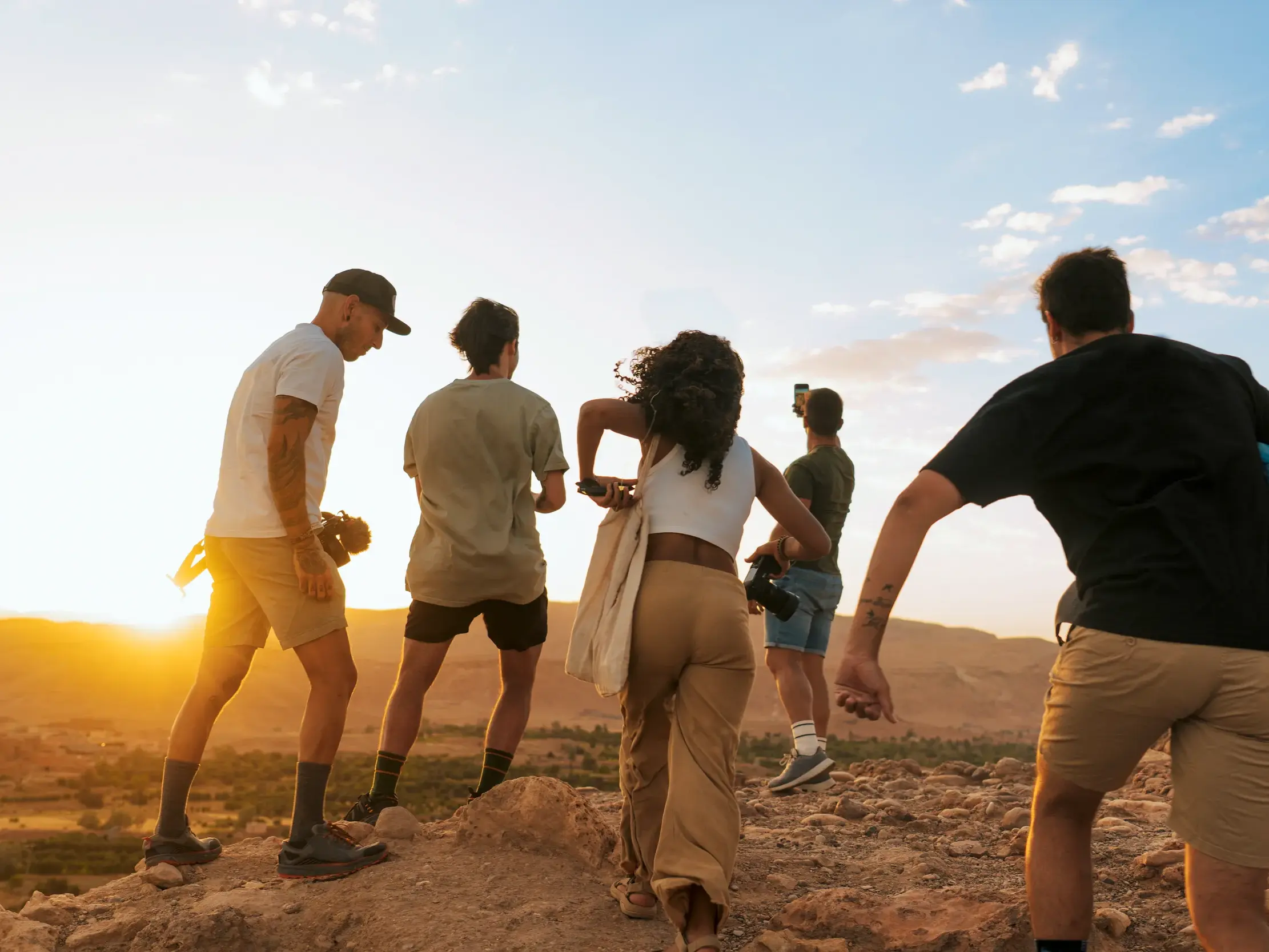 Eine junge Reisegruppe blickt bei Sonnenuntergang von einem Hügel auf die berühmte Lehmstadt Ait Benhaddou in Marokko.