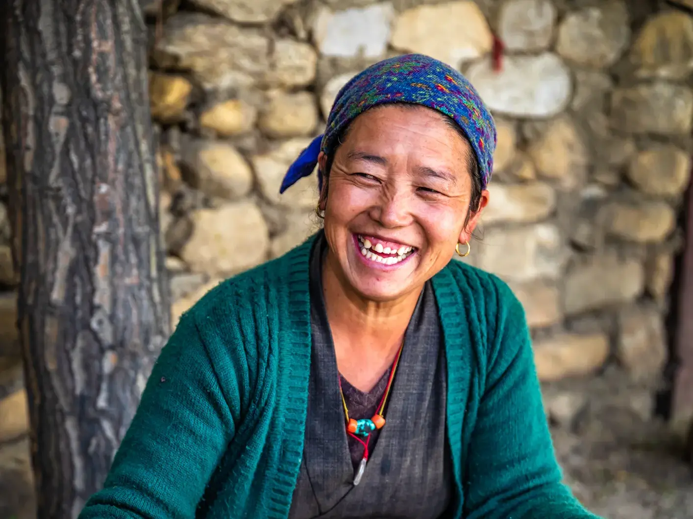Eine herzlich lachende tibetische Frau mit buntem Kopftuch. Authentische Begegnung auf einer Rundreise durch Tibet.