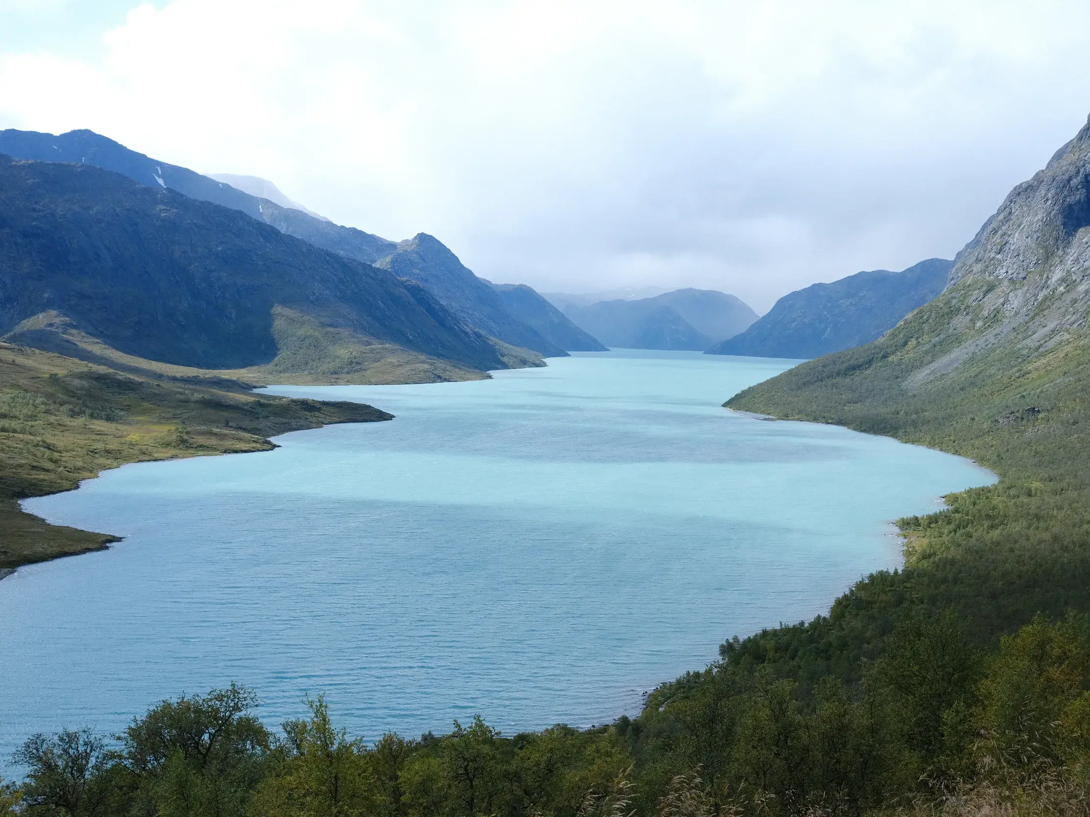Panoramablick auf den türkisfarbenen Gjende-See, umgeben von der Berglandschaft des Jotunheimen Nationalparks in Norwegen.