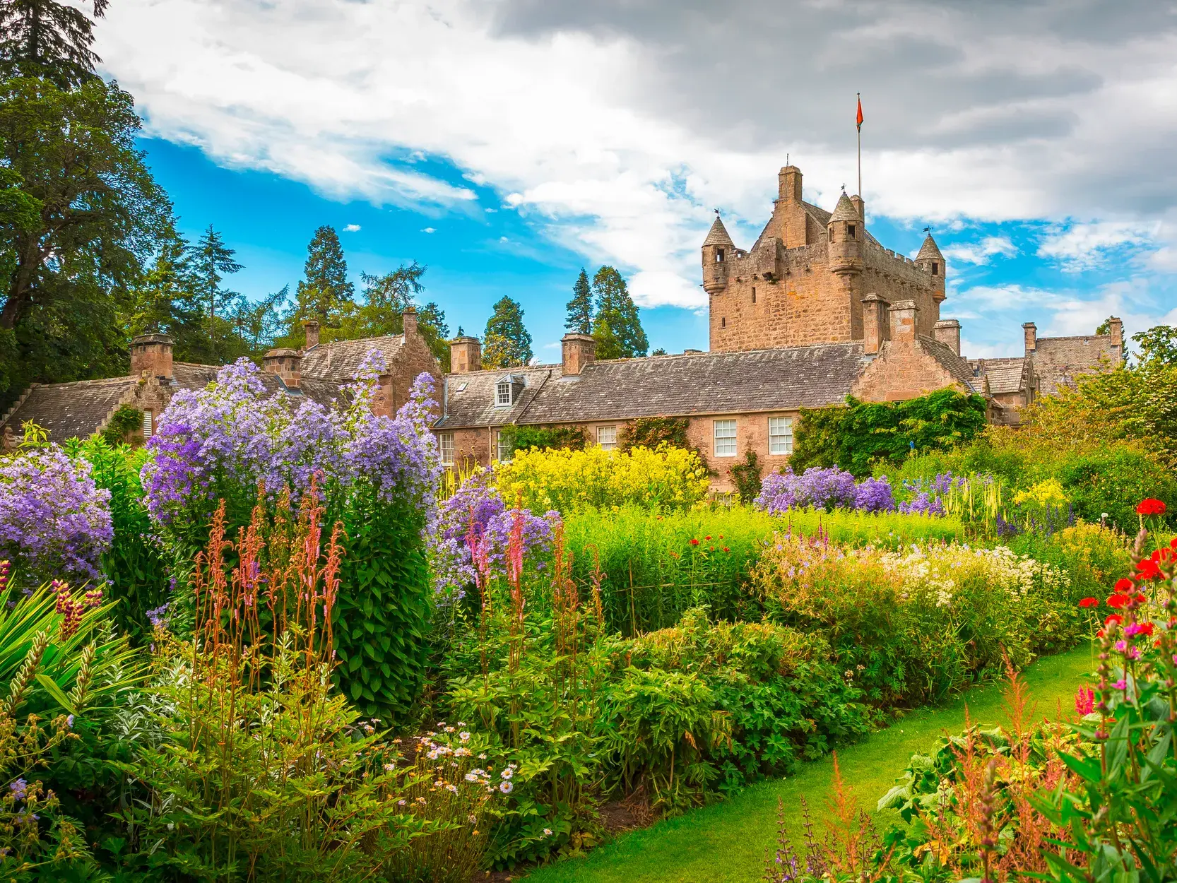 Der traumhafte Garten von Cawdor Castle in Schottland mit farbenfrohen Blumen und Blick auf die historische Burganlage.