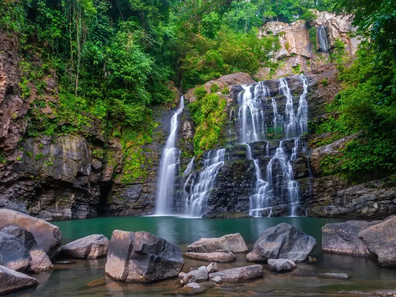Der kaskadierende Nauyaca Wasserfall stürzt über Felsen in ein türkises Becken, umgeben von tropischem Regenwald in Costa Rica.