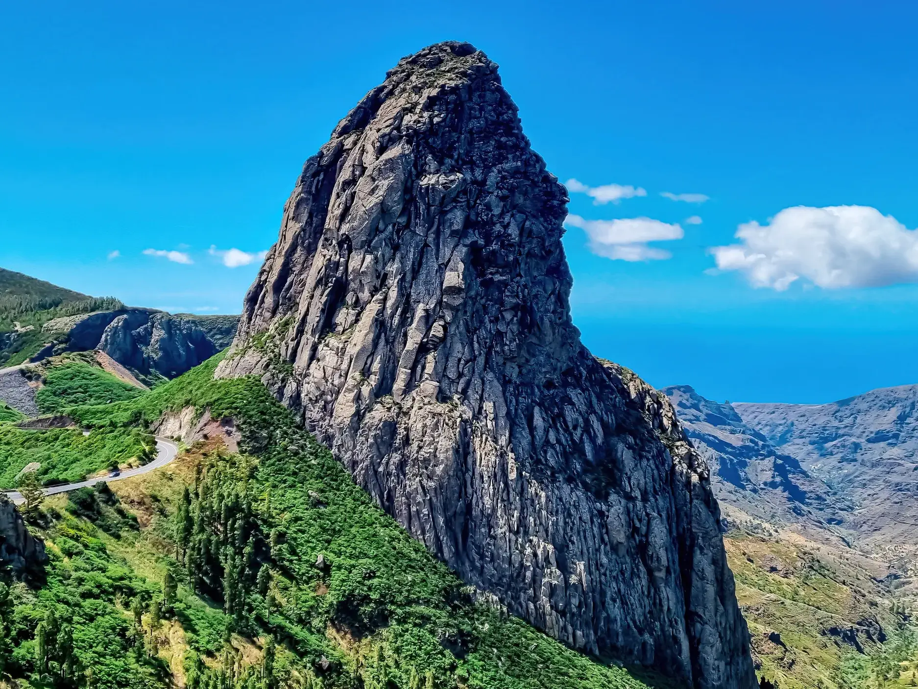 Der markante Felsen Roque de Agando, ein Wahrzeichen auf La Gomera, in grüner Berglandschaft unter blauem Himmel.
