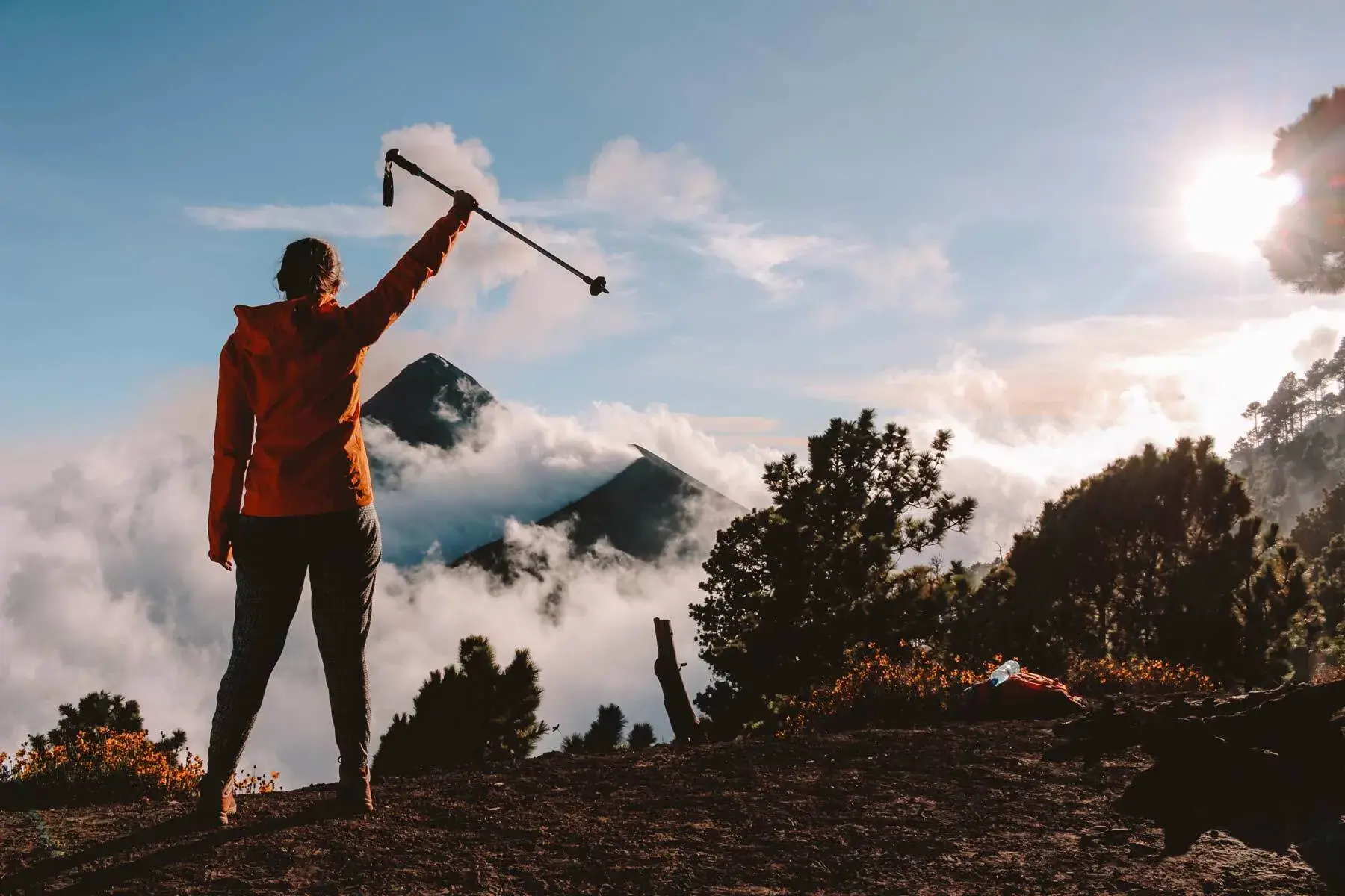 Eine Wanderin jubelt bei Sonnenaufgang auf dem Gipfel des Vulkans Acatenango und blickt über ein Meer aus Wolken.