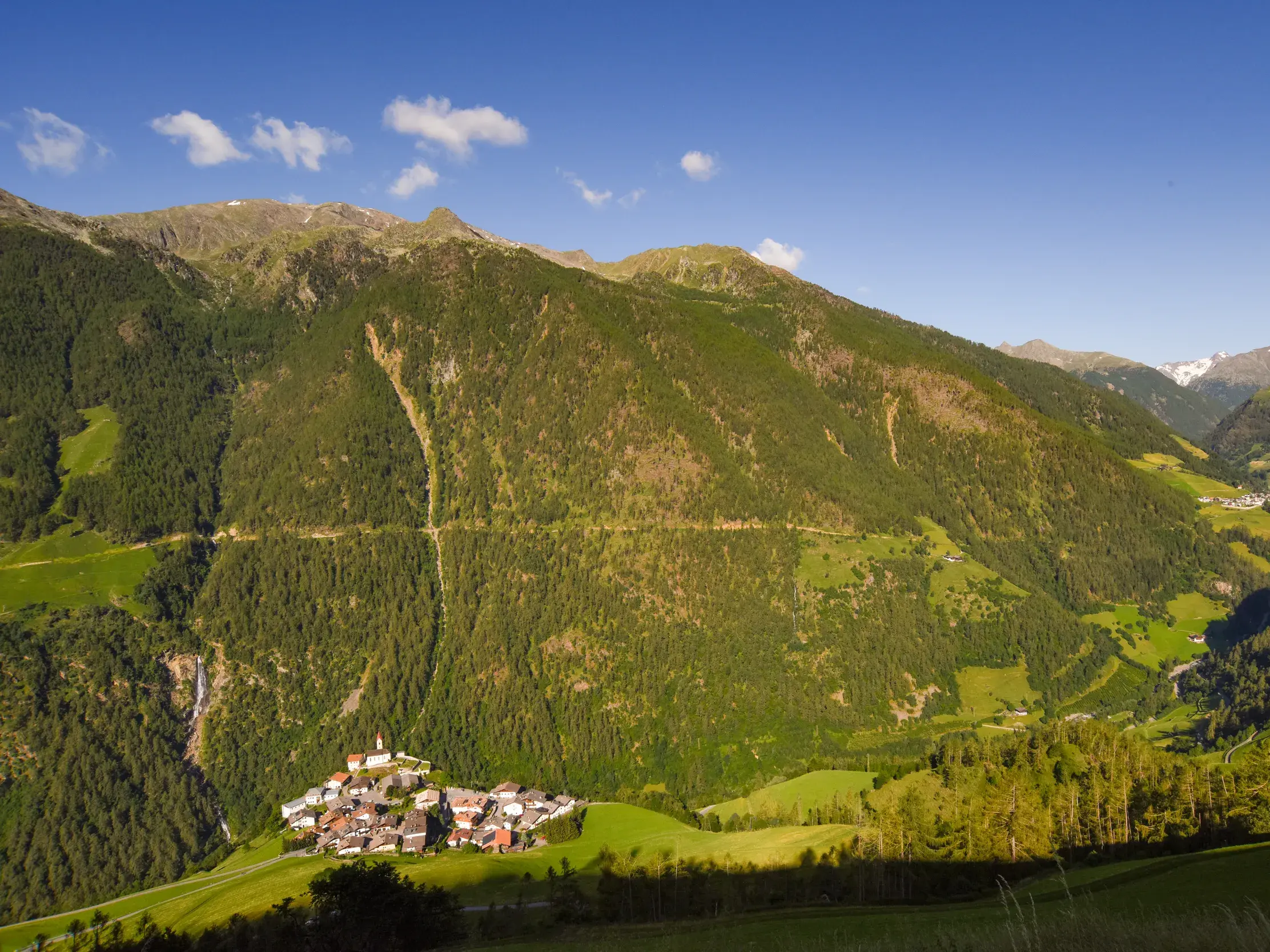 Sonniger Blick vom Meraner Höhenweg auf das Bergdorf Katharinaberg, eingebettet in die bewaldeten Hänge der Texelgruppe.
