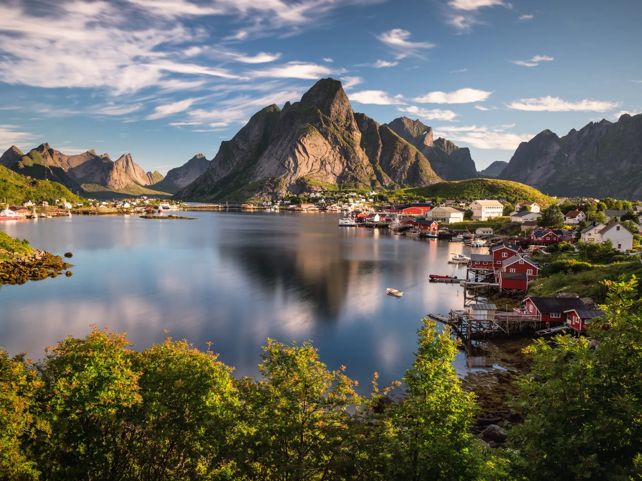 Malerisches Fischerdorf Reine auf den norwegischen Lofoten mit roten Holzhäusern an einem Fjord, überragt von spitzen Bergen.