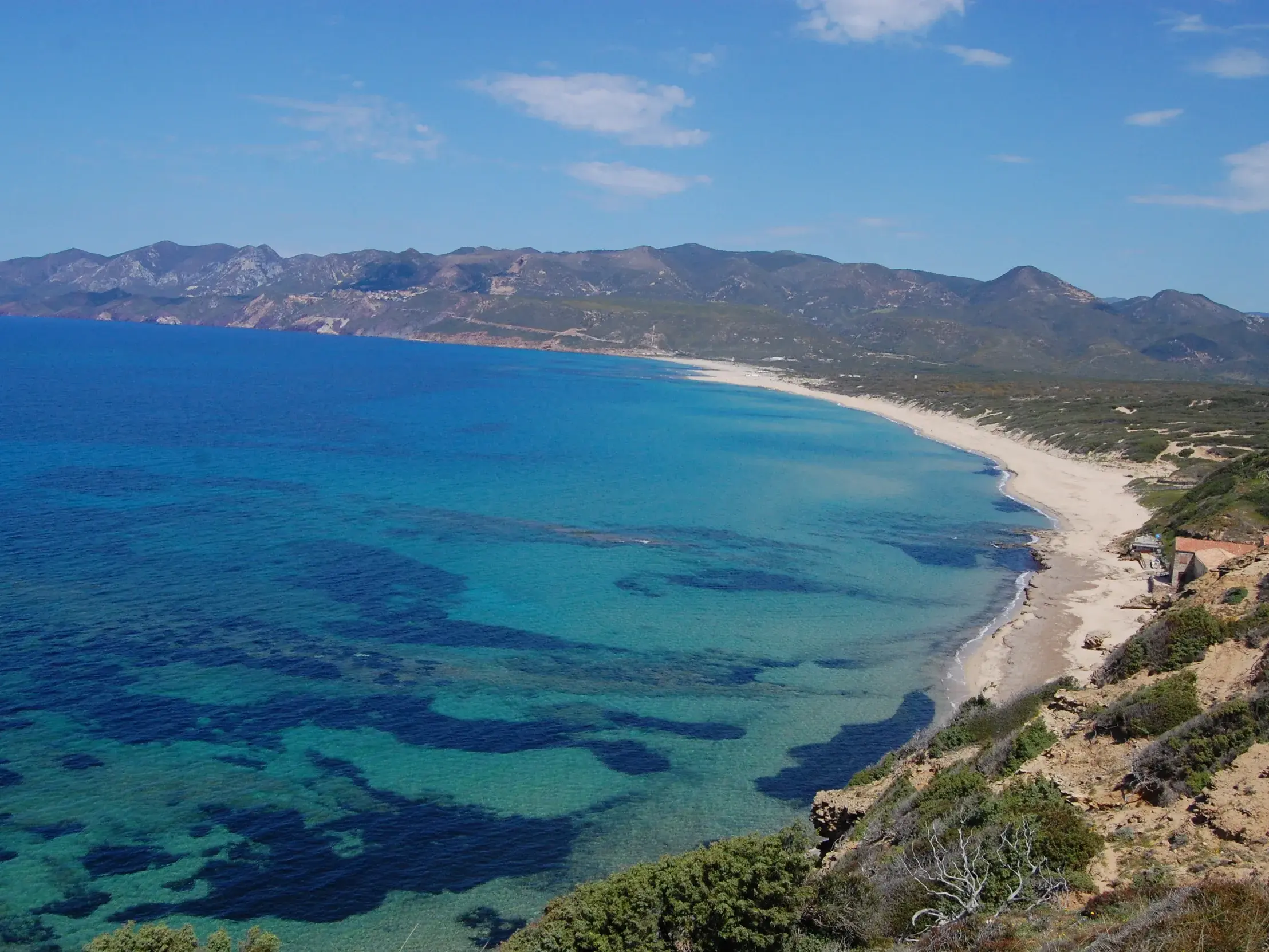 Panoramablick einer Küstenwanderung auf den langen Sandstrand von Portixeddu und das türkisblaue Meer im Süden Sardiniens.