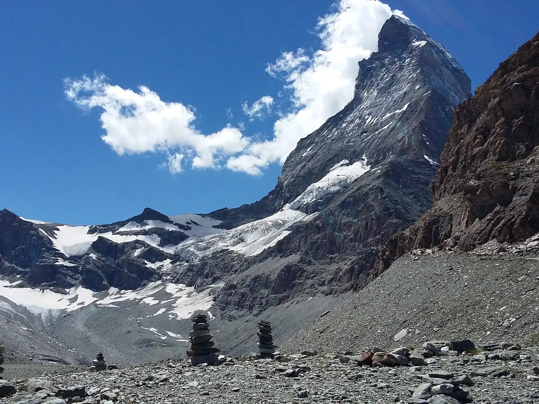 Steinmännchen im Geröllfeld am Hörnliweg mit Blick auf den Gipfel des schneebedeckten Matterhorns bei Zermatt.
