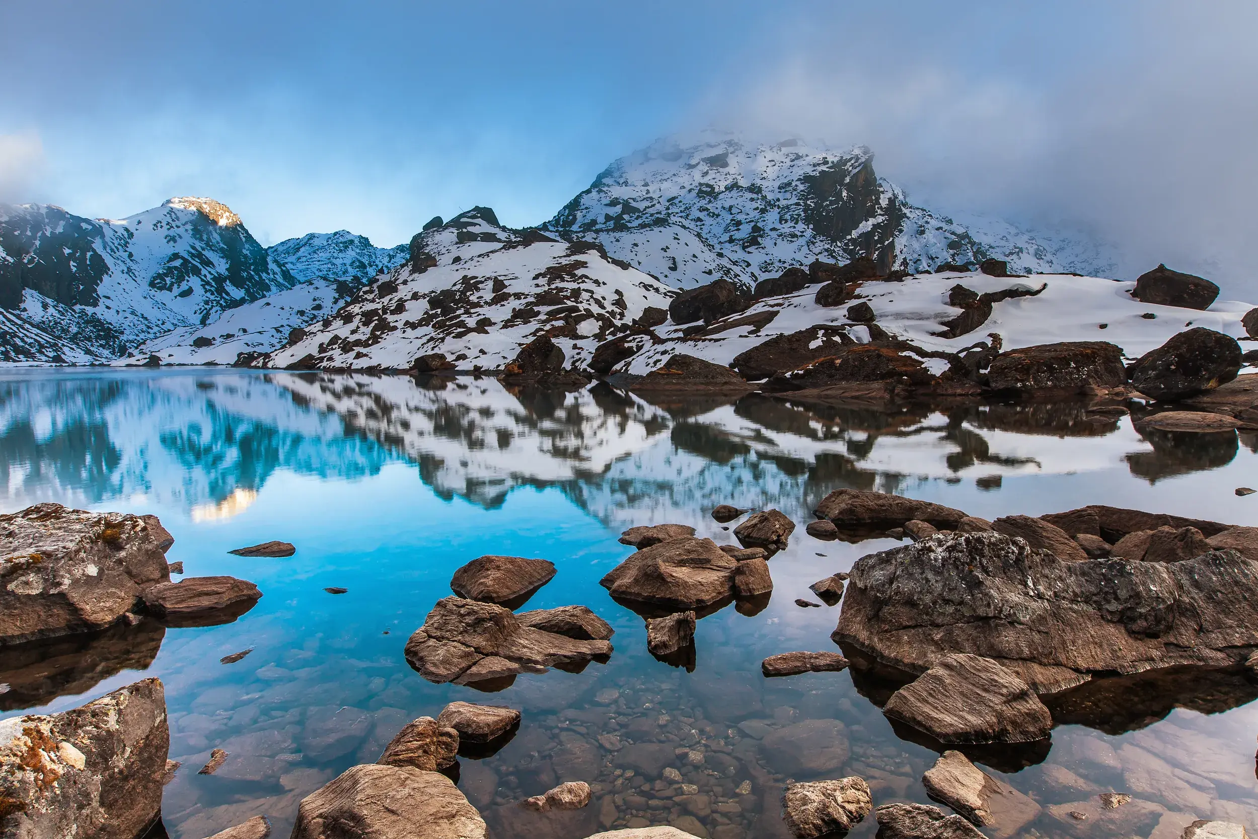 Beim Trekking im Langtang-Nationalpark spiegeln sich schneebedeckte Gipfel im kristallklaren Gosainkund See in Nepal.