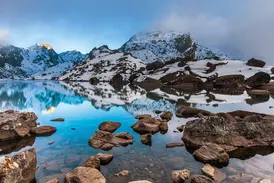 Beim Trekking im Langtang-Nationalpark spiegeln sich schneebedeckte Gipfel im kristallklaren Gosainkund See in Nepal.