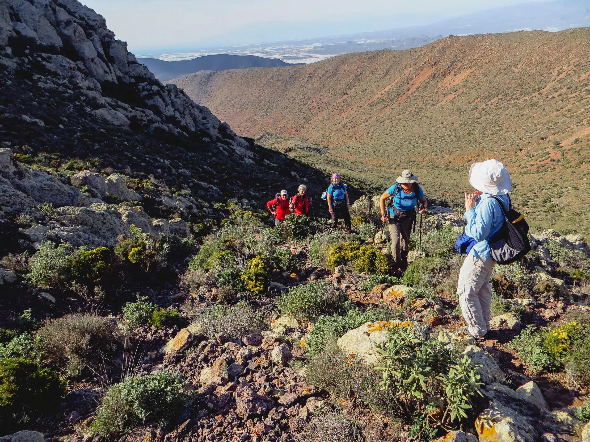 Eine kleine Wandergruppe erklimmt einen felsigen Pfad in der hügeligen, kargen Vulkanlandschaft des Naturparks Cabo de Gata.