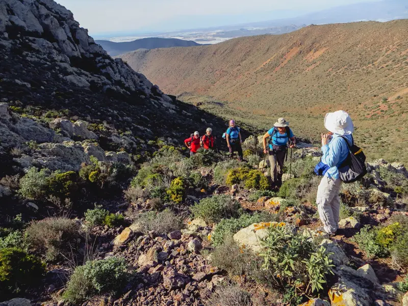 Eine kleine Wandergruppe erklimmt einen felsigen Pfad in der hügeligen, kargen Vulkanlandschaft des Naturparks Cabo de Gata.