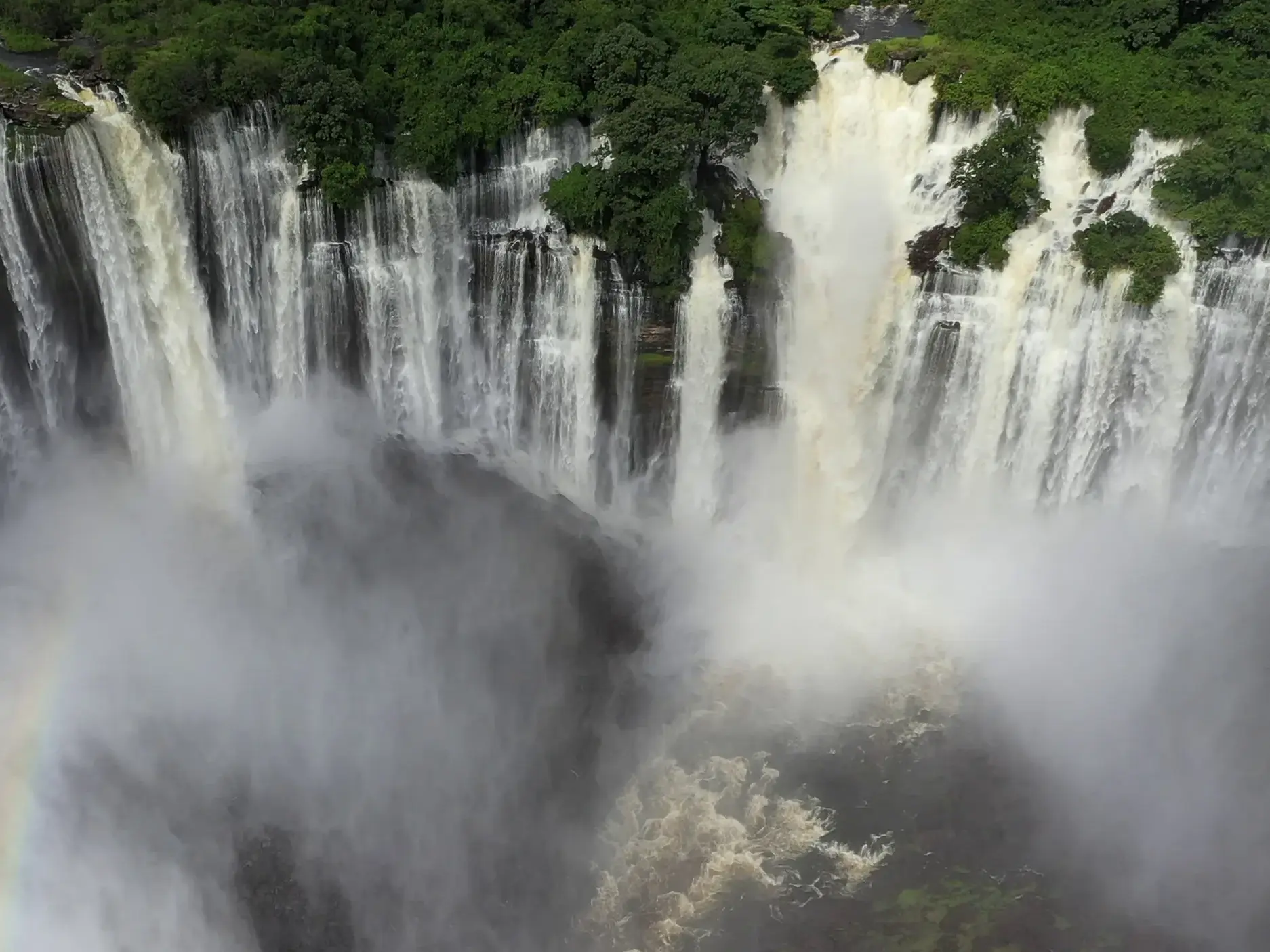 Die rauschenden Quedas de Kalandula in Angola, wo der Lucala-Fluss über eine breite, grüne Klippe in eine neblige Schlucht stürzt.