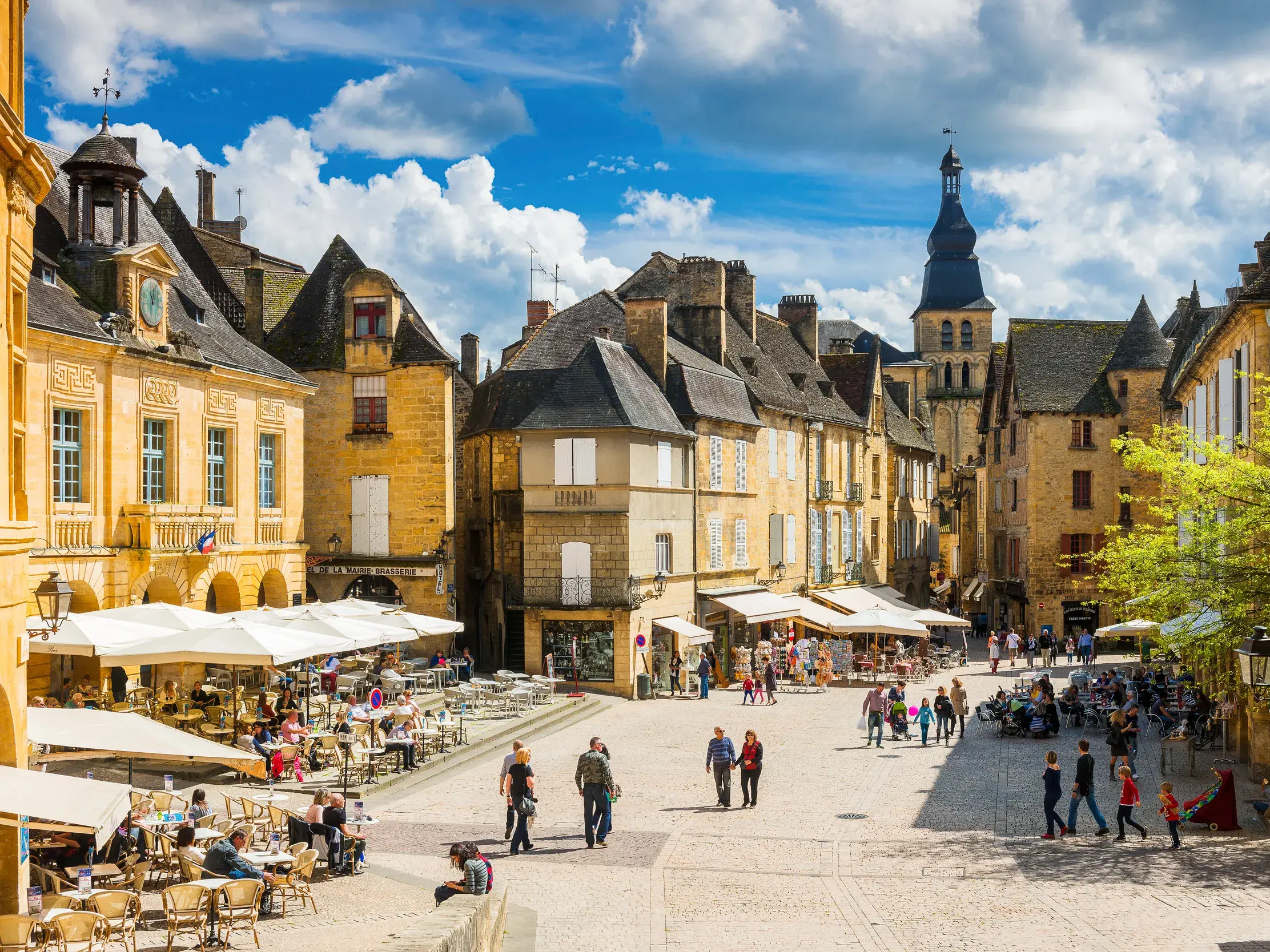 Lebhafter Platz in der Renaissancestadt Sarlat mit Besuchern in Straßencafés vor historischen Sandsteingebäuden.