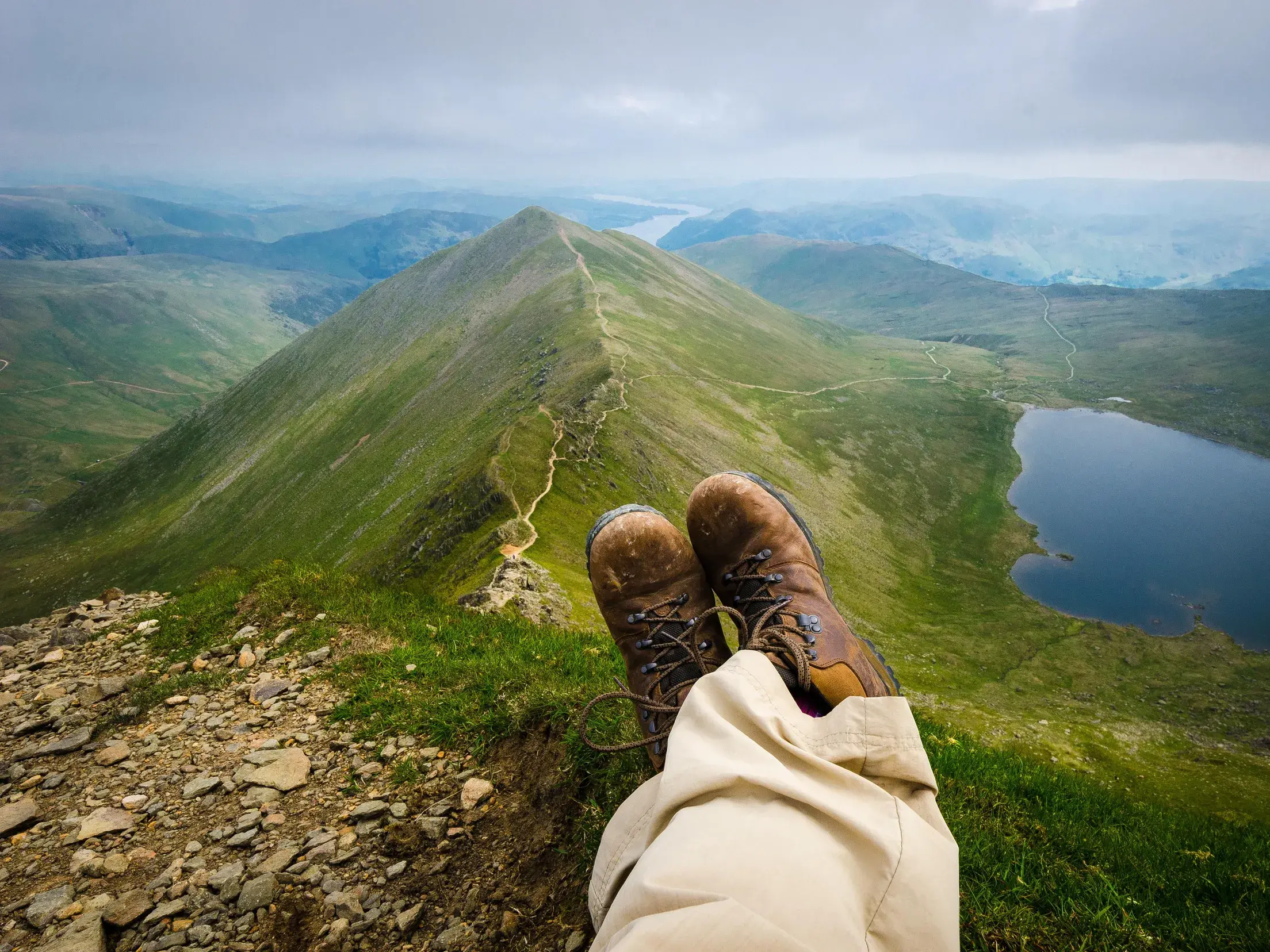 Wanderpause auf einem Gipfel im Lake District mit Blick über einen schmalen Grat, einen Bergsee und grüne Täler.