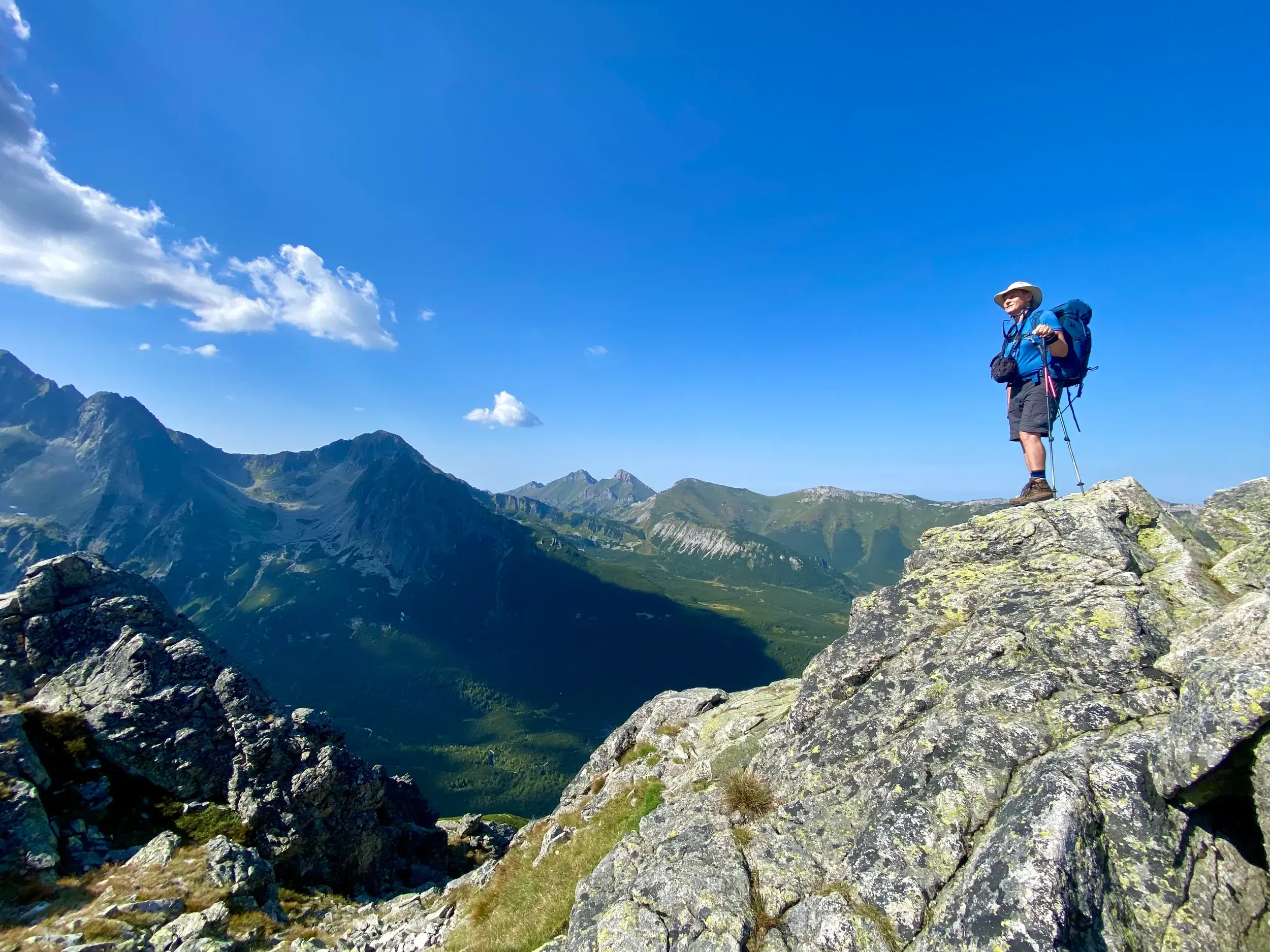 Ein Wanderer mit Rucksack und Stöcken steht auf einem Felsgipfel und blickt auf die beeindruckende Bergkette der Hohen Tatra.