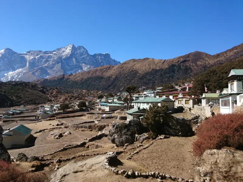 Weite Aussicht über das Sherpa-Dorf Khumjung mit seinen Terrassenfeldern vor den schneebedeckten Gipfeln des Himalaya.
