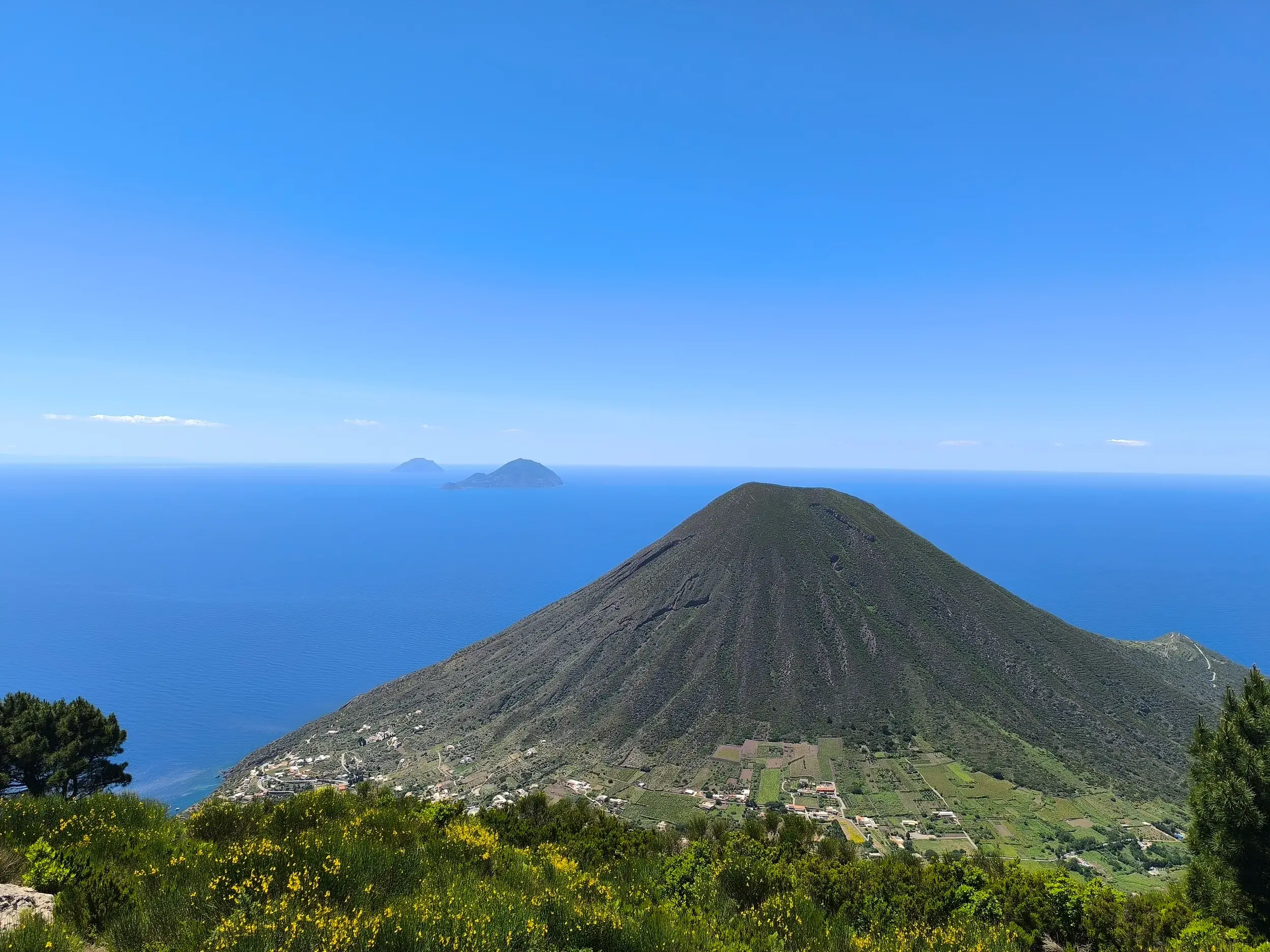 Aussicht vom Wanderweg auf Lipari über die grüne Vulkaninsel Salina mit den Inseln Filicudi und Alicudi am Horizont.