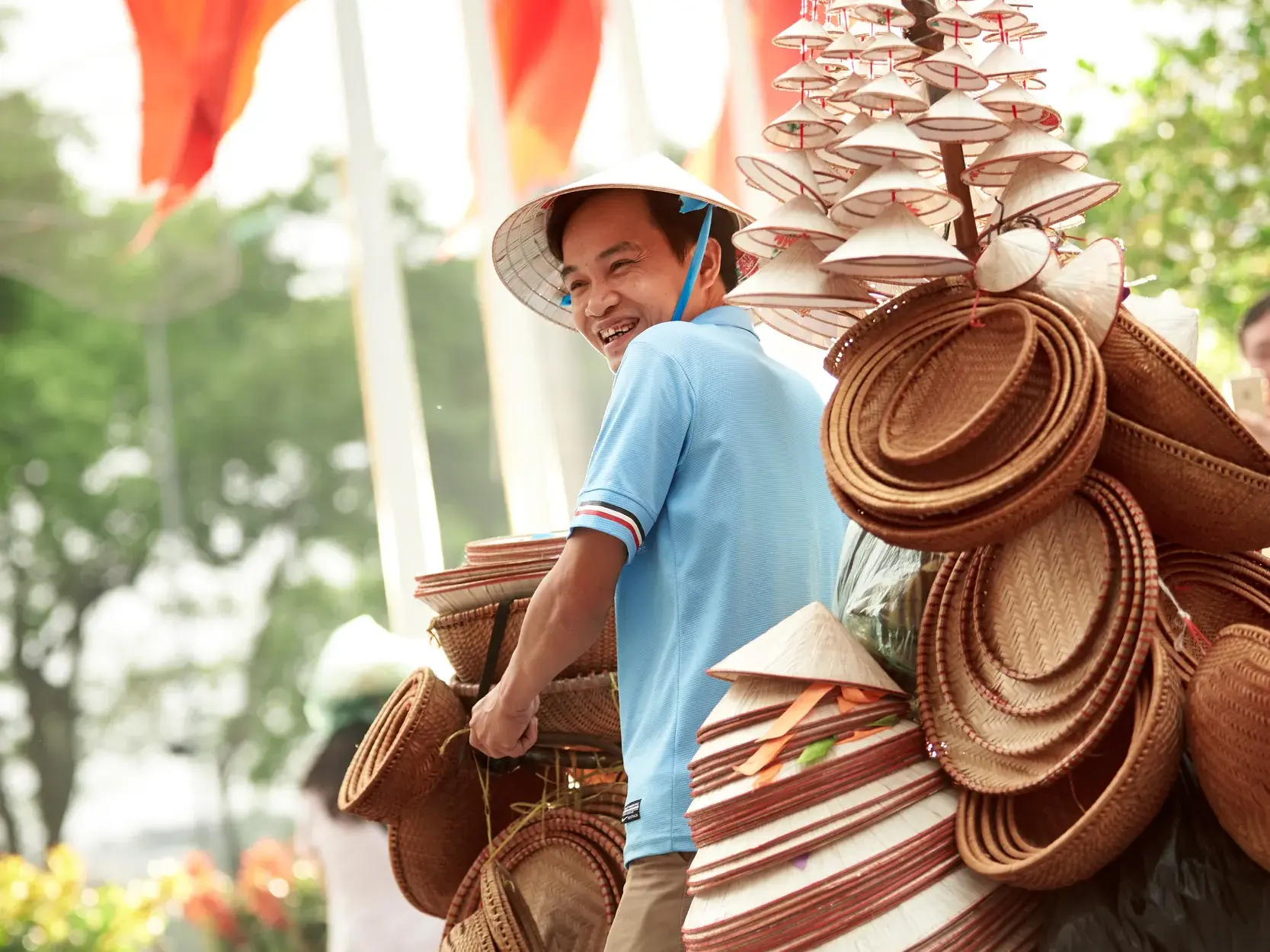 Begegnung auf einer Studiosus-Studienreise: Ein lachender Mann verkauft traditionelle Kegelhüte und Korbwaren in Vietnam.
