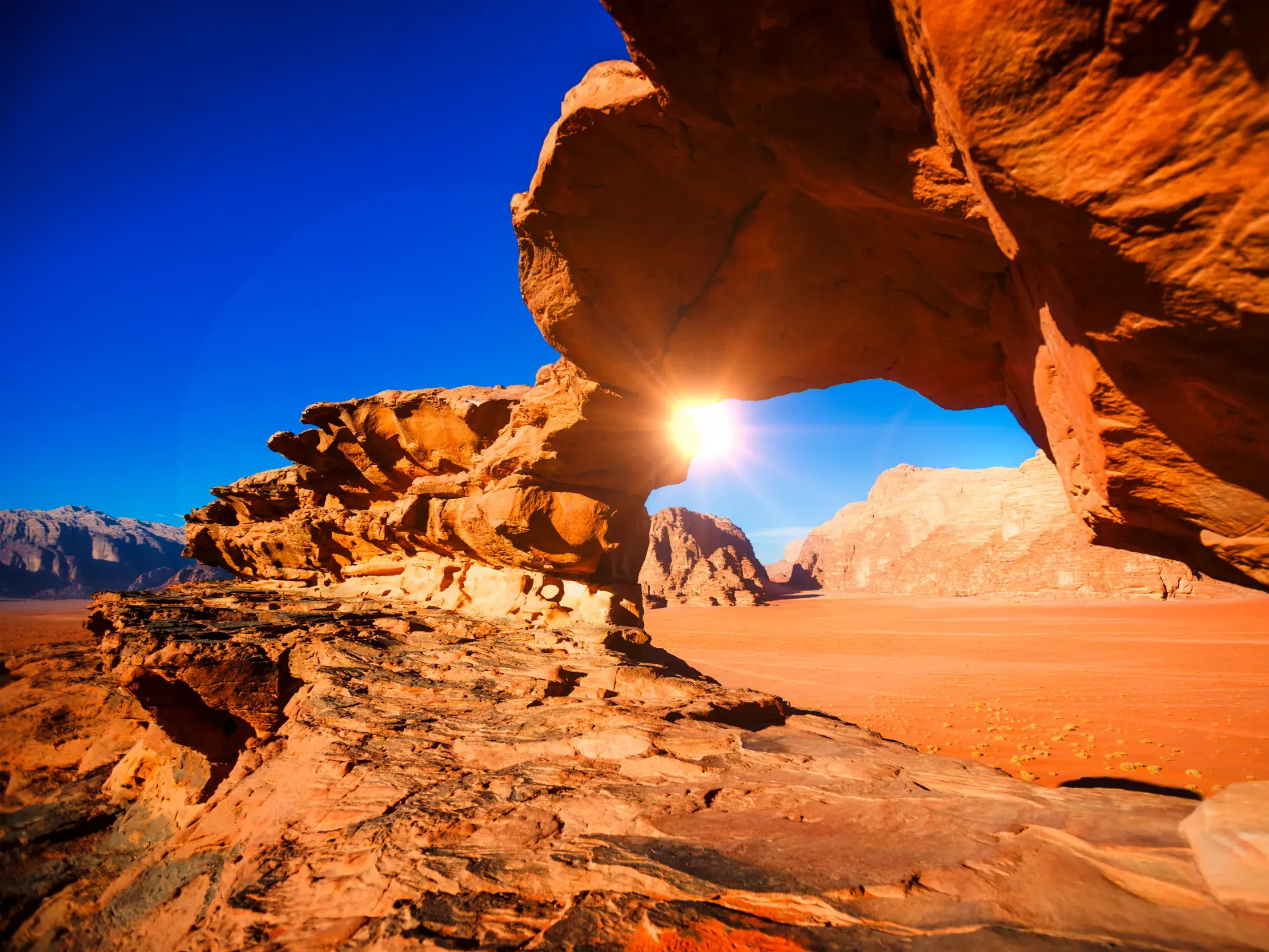 Untergehende Sonne scheint durch einen roten Felsbogen in der weiten Wüstenlandschaft des Wadi Ram in Jordanien.