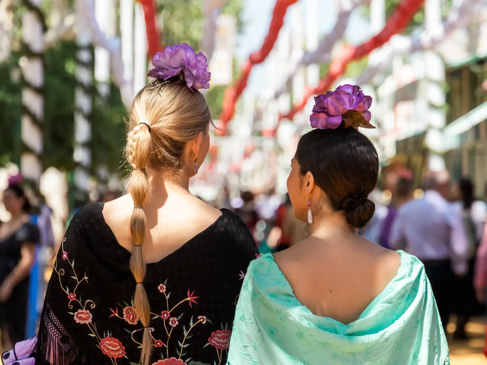 Rückansicht zweier Frauen, die bunte, floral bestickte Umhängetücher über ihrer traditionellen Tracht in Andalusien tragen.