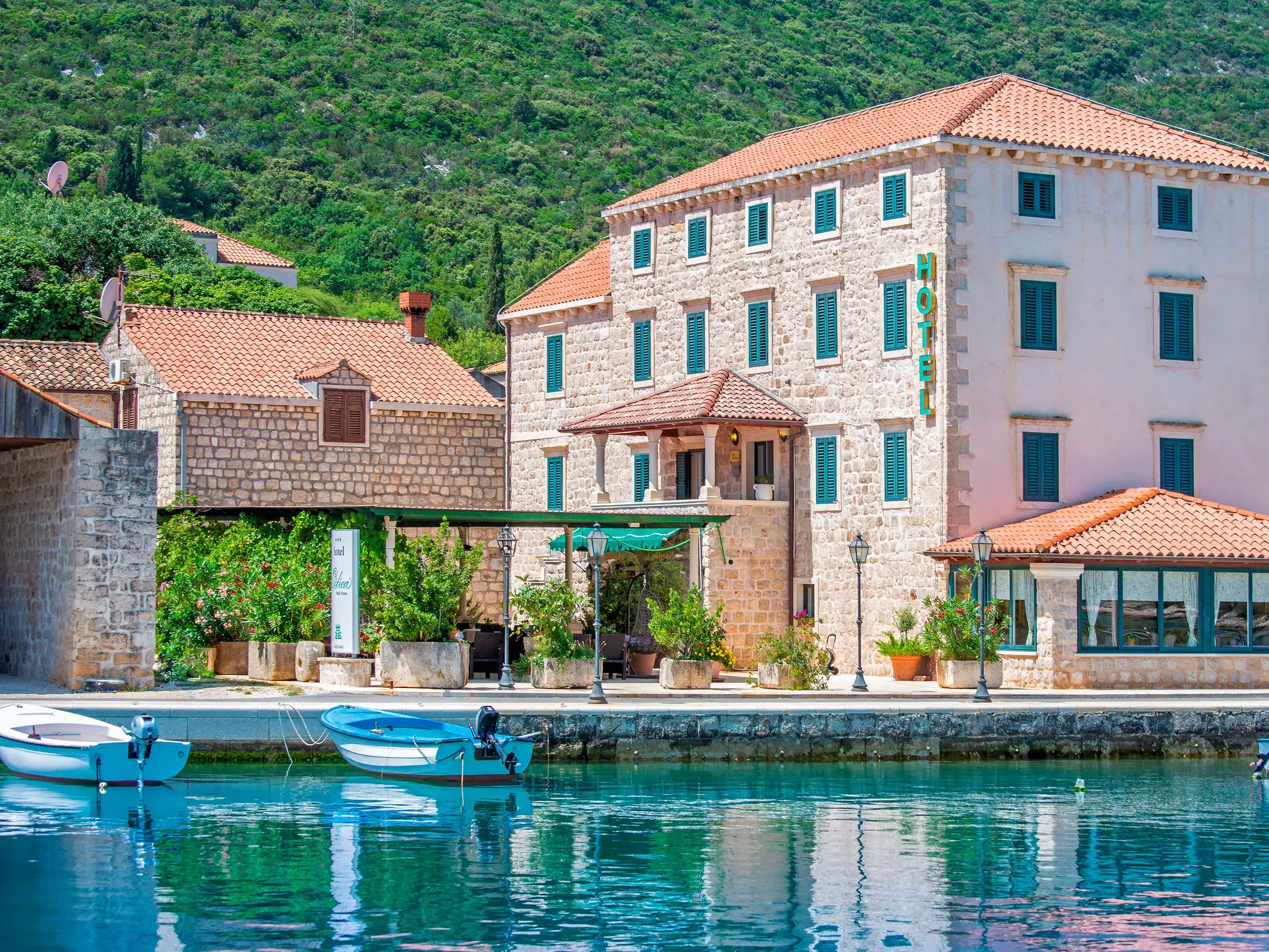 Das charmante Hotel Ostrea mit Steinfassade direkt am Hafen von Mali Ston, davor liegen kleine Boote im klaren Wasser der Adria.