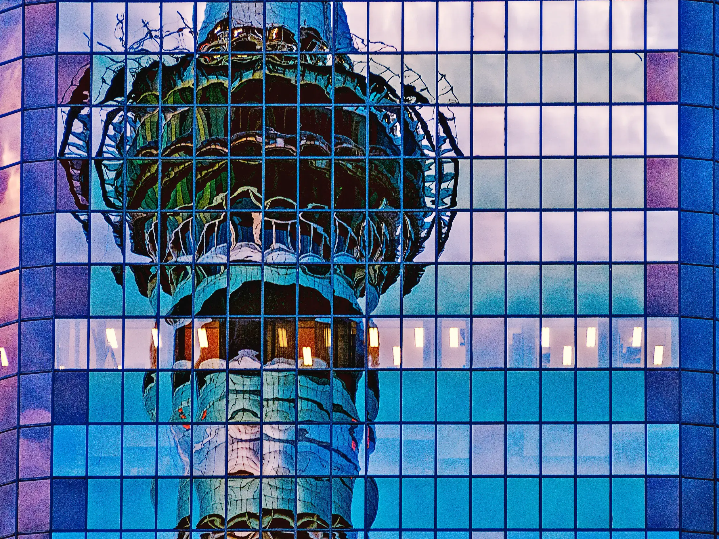 Spiegelung des Auckland Sky Tower in der blauen, gekachelten Glasfassade eines modernen Gebäudes bei Dämmerung.