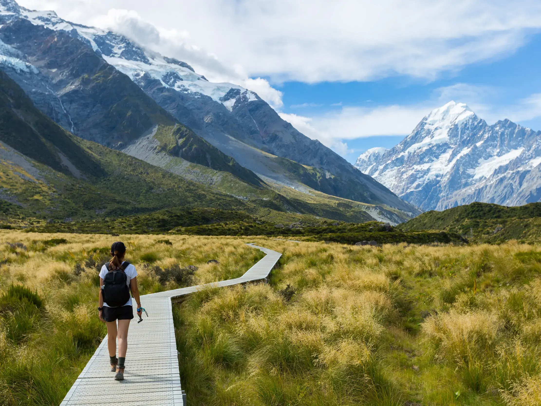Eine Frau wandert auf dem hölzernen Hooker Valley Track mit Blick auf den schneebedeckten Mount Cook in Neuseelands Südalpen.