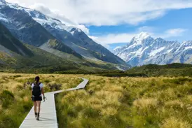 Eine Frau wandert auf dem hölzernen Hooker Valley Track mit Blick auf den schneebedeckten Mount Cook in Neuseelands Südalpen.
