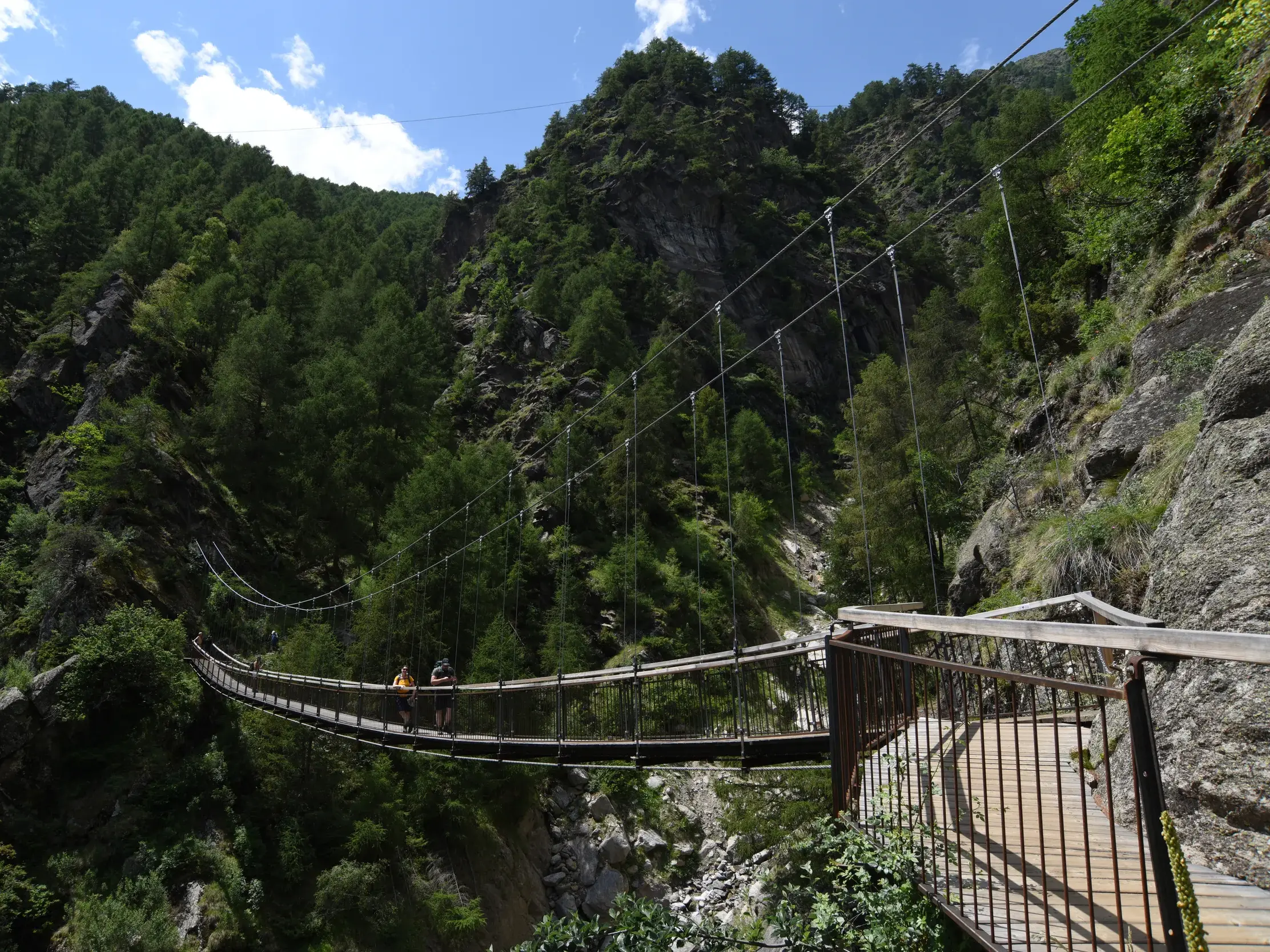Zwei Wanderer auf dem Meraner Höhenweg überqueren eine Hängebrücke in der 1000-Stufenschlucht im Naturpark Texelgruppe.
