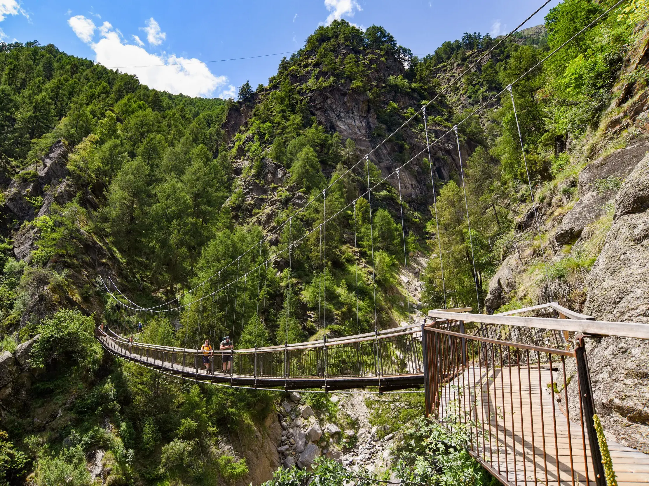 Zwei Wanderer überqueren die lange, luftige Hängebrücke in der 1000-Stufen-Schlucht im Naturpark Texelgruppe in Südtirol.
