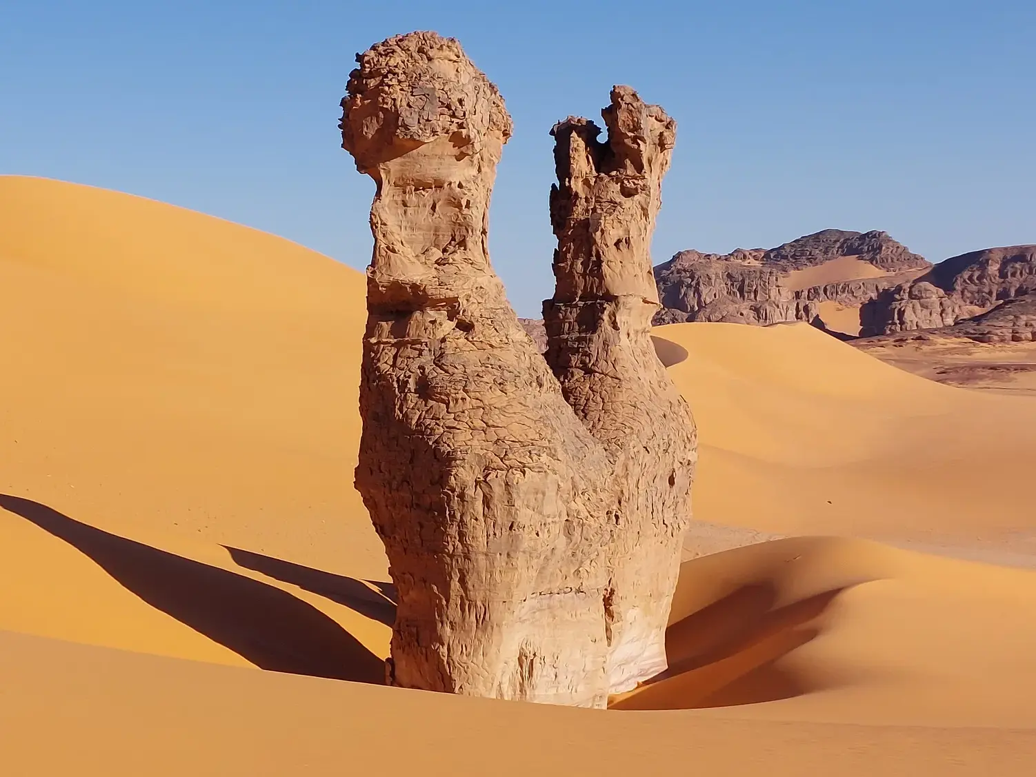 Die berühmten Twin Towers der Sahara, zwei Felstürme in der Tadrart-Wüste in Algerien umgeben von roten Sanddünen.