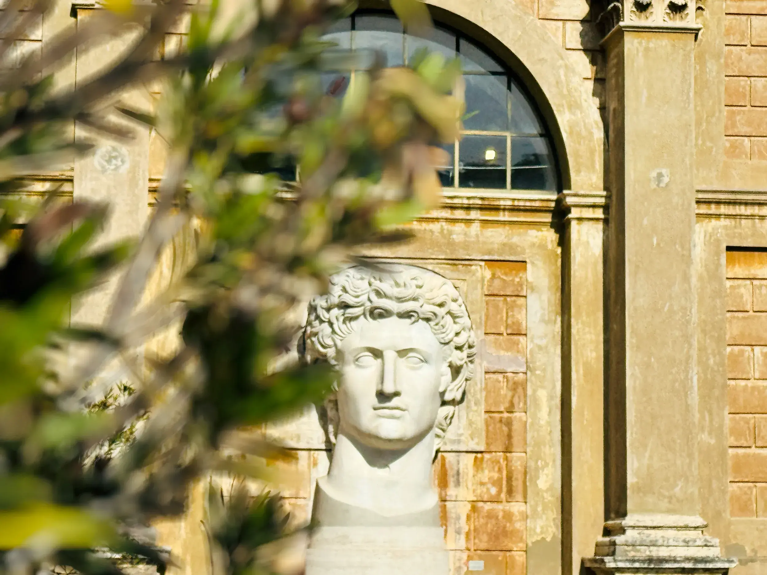 Antike Marmorbüste mit Locken vor der sonnigen Steinfassade eines Gebäudes der Vatikanischen Museen in Rom.