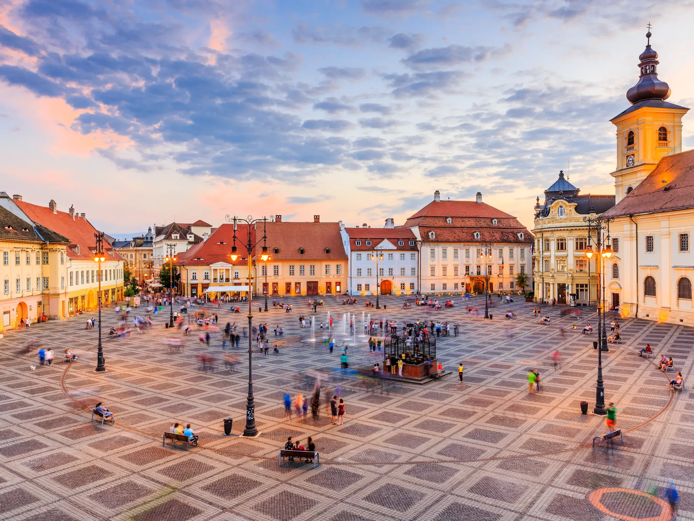 Das einzigartige Ensemble der Altstadt von Hermannstadt mit historischen Patrizierhäusern und belebtem Platz bei Sonnenuntergang.