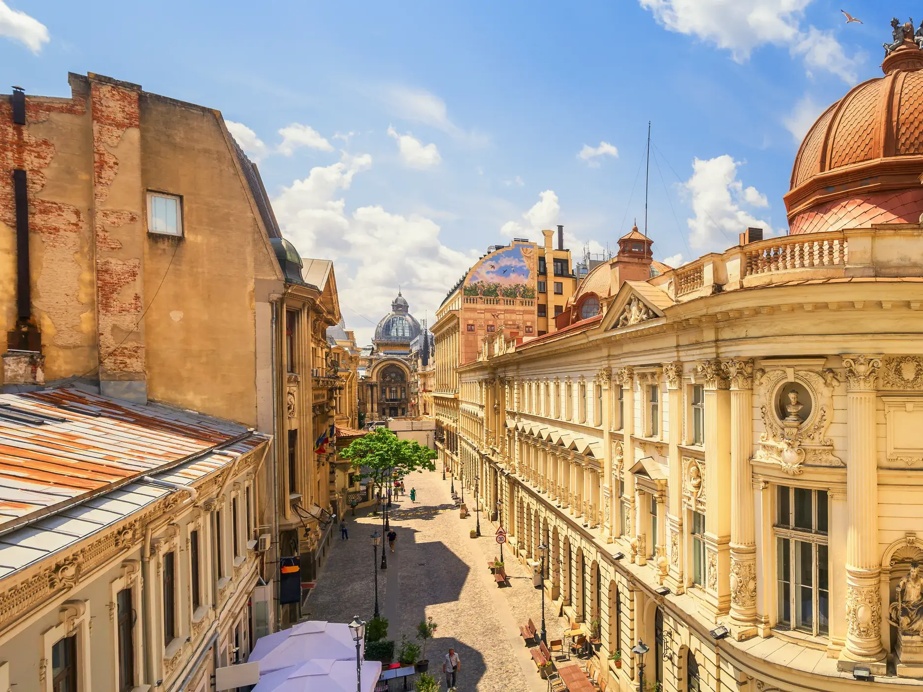 Erhöhter Blick auf eine Gasse der Altstadt von Bukarest, gesäumt von prachtvollen historischen Fassaden unter blauem Himmel.