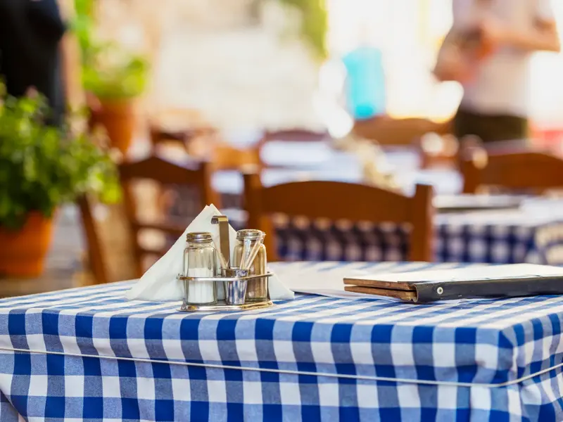Einladend gedeckter Tisch in einer typisch griechischen Taverne, bereit für landestypische Köstlichkeiten wie Mezedes.